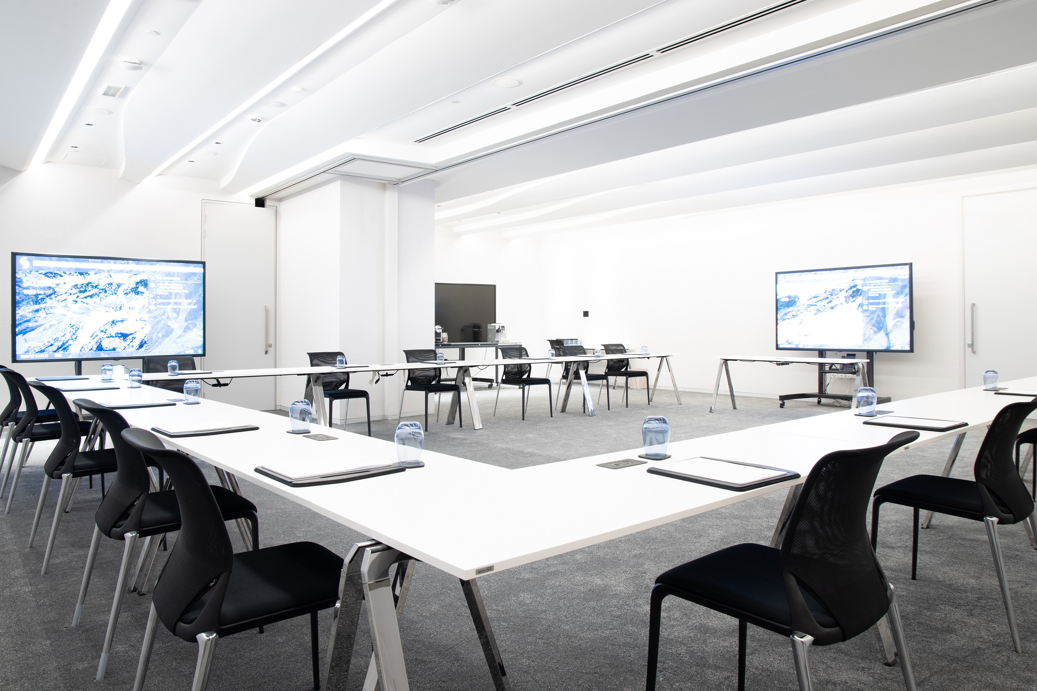 Modern U-shaped conference room with black chairs and dual display screens.