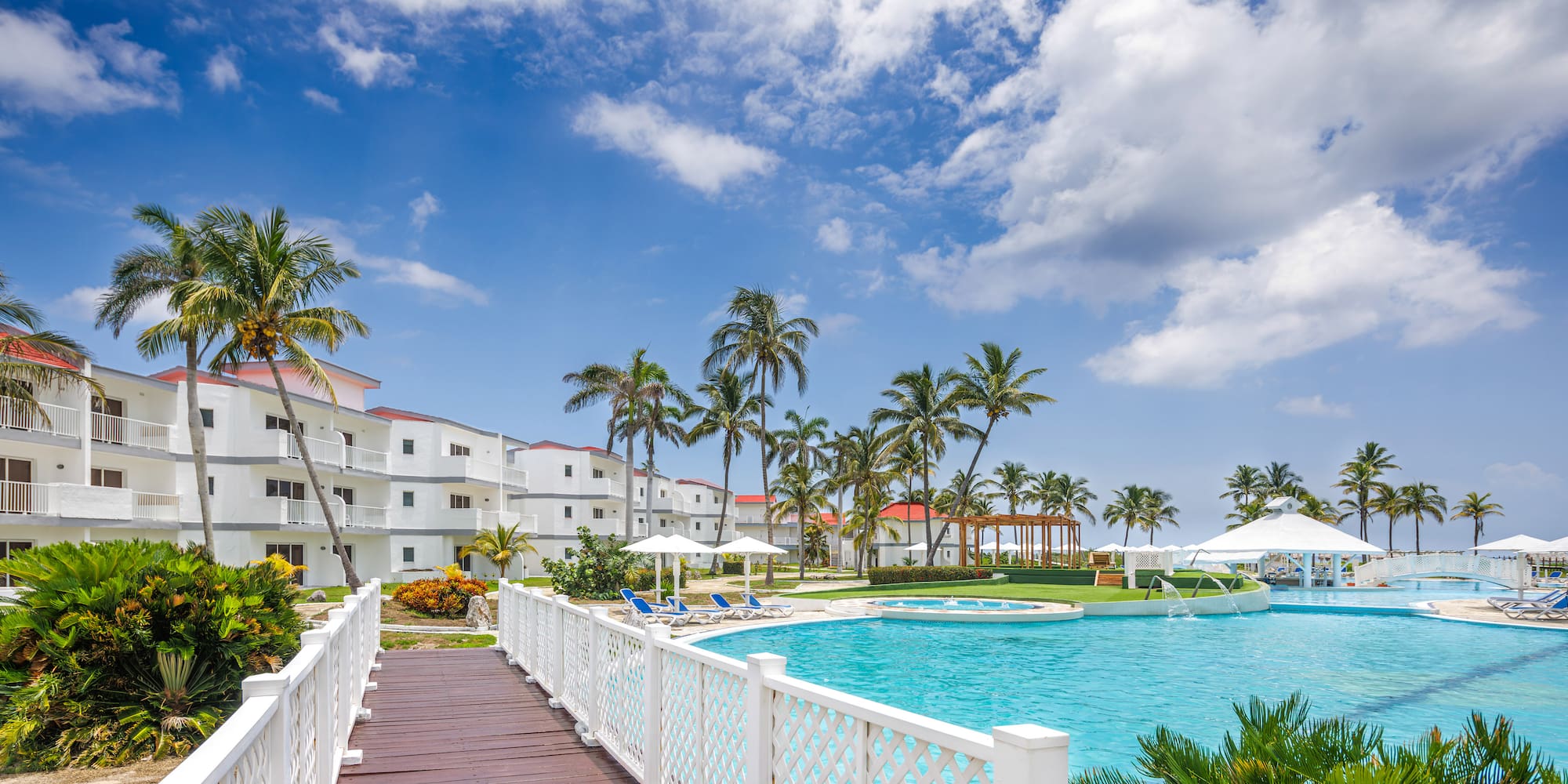 a bridge over a pool with palm trees and buildings