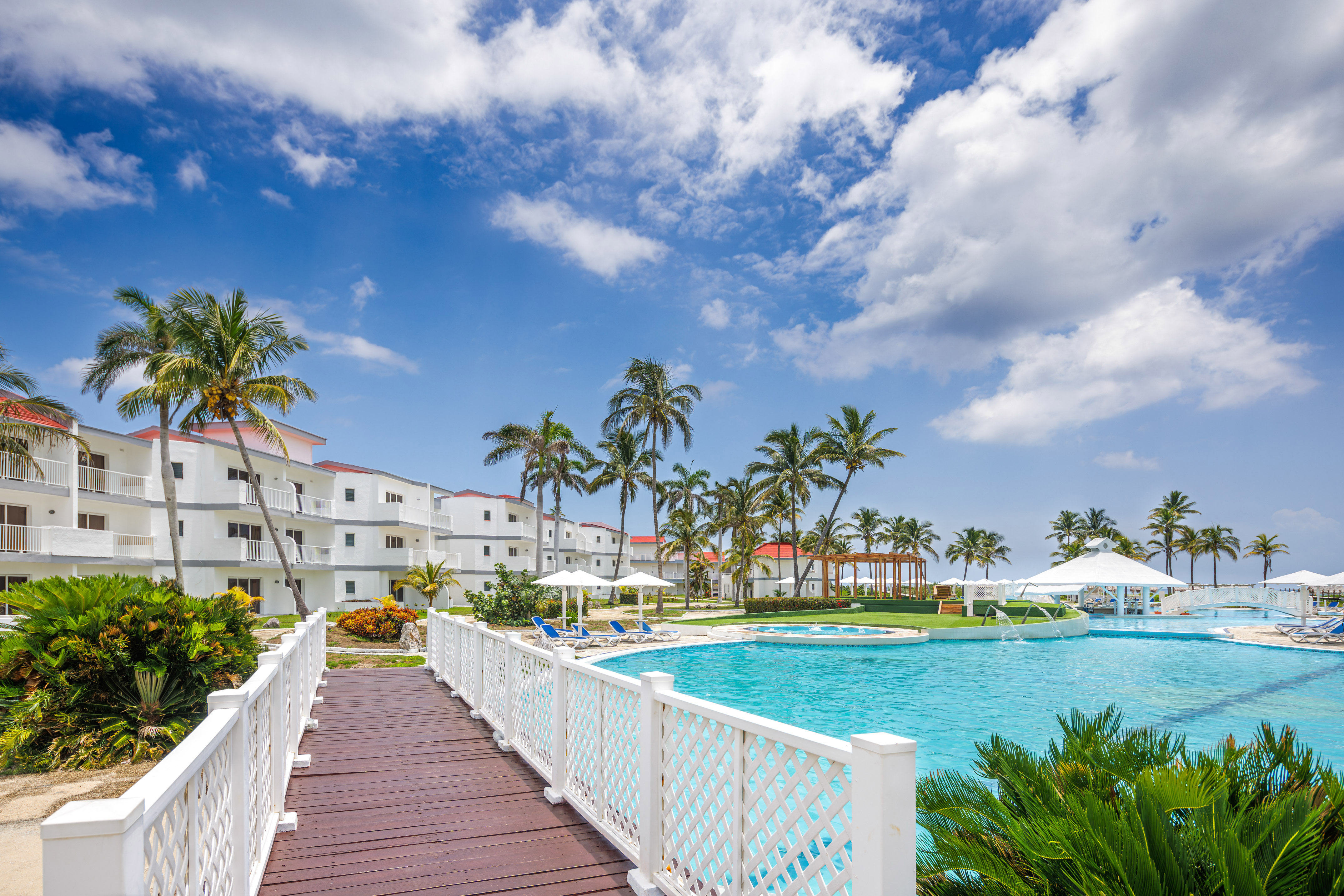 a bridge over a pool with palm trees and buildings