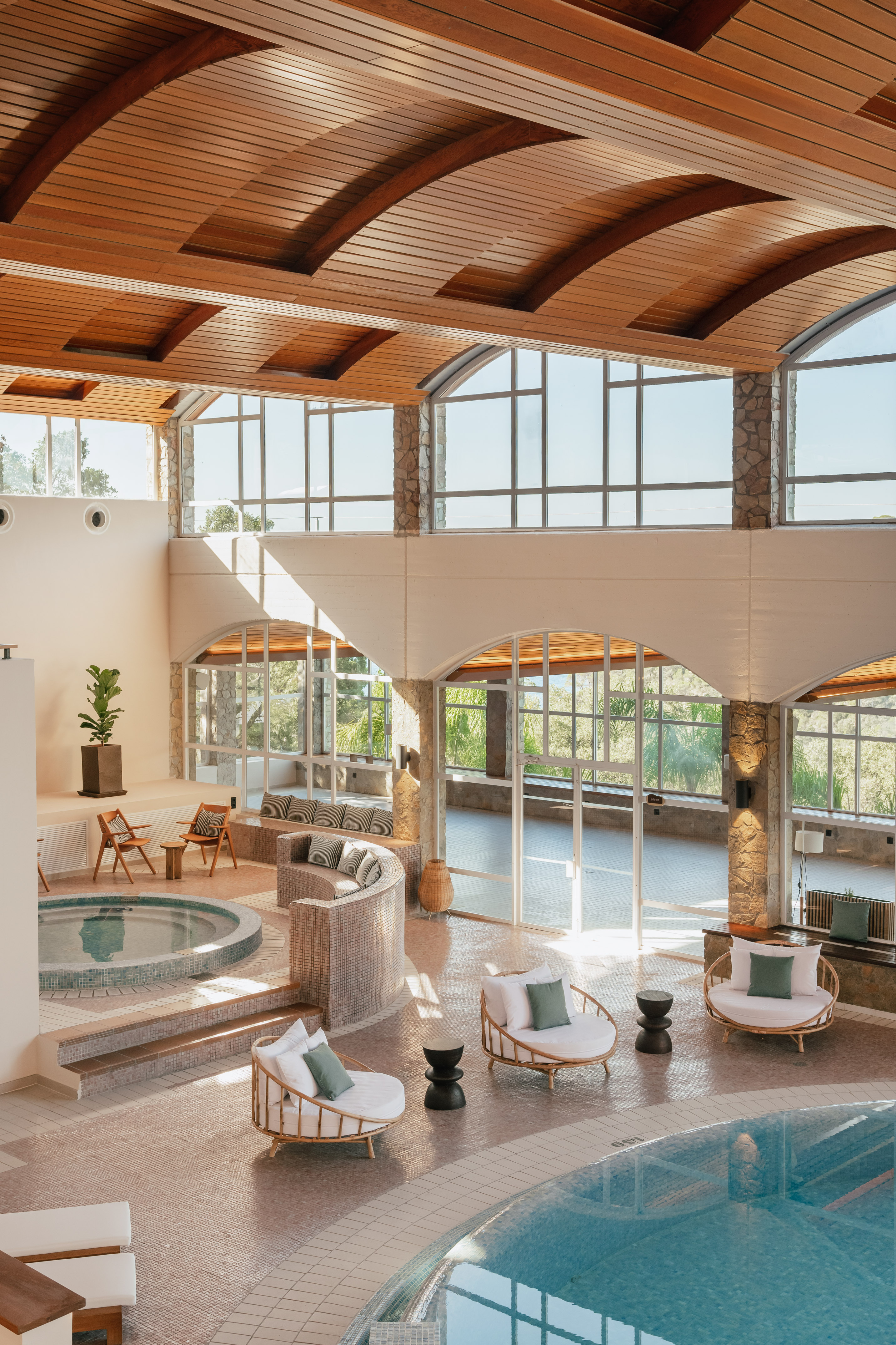 Indoor spa with pool, hot tub, modern seating, and arched wooden ceiling.