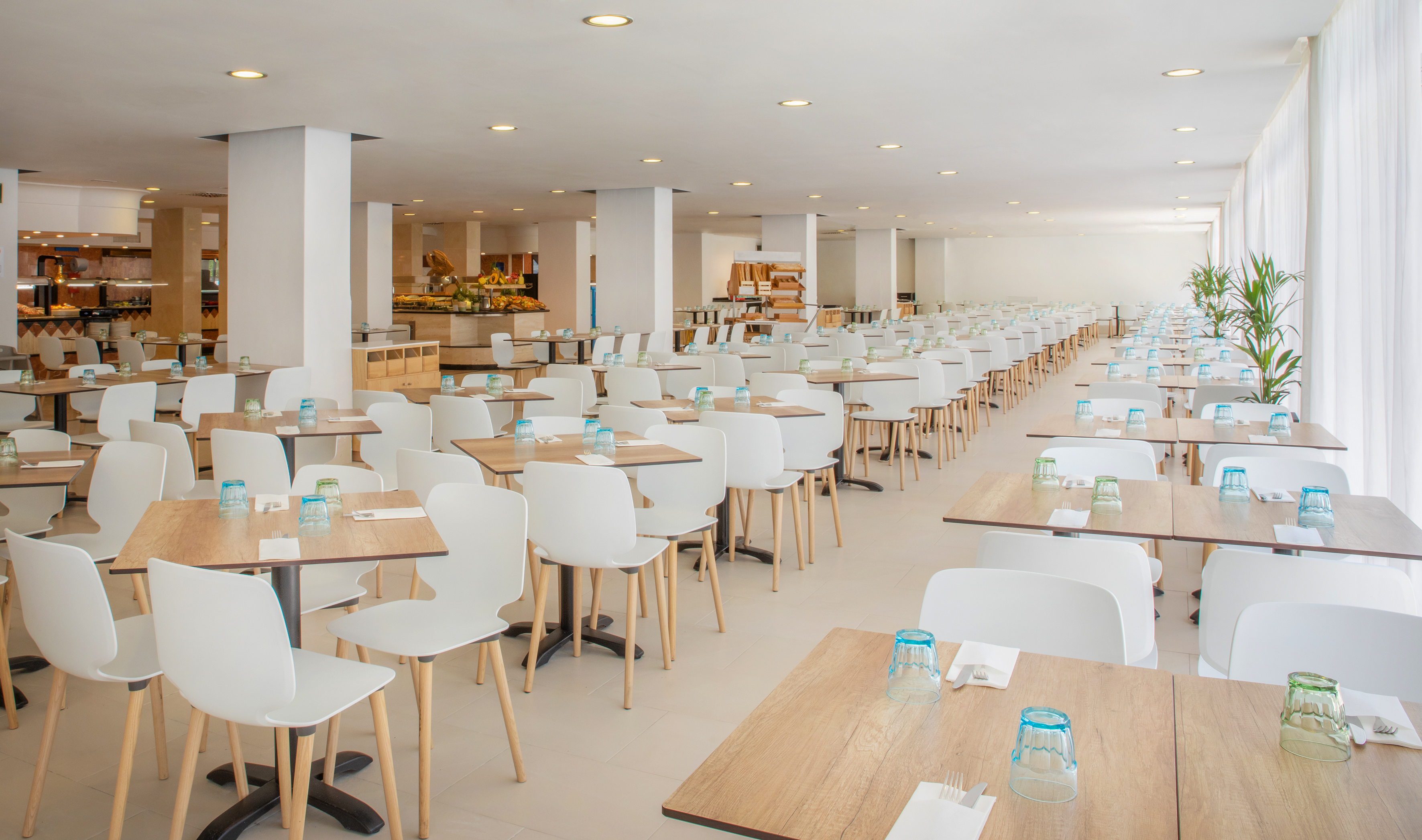 Spacious modern buffet restaurant with many empty tables and white chairs.