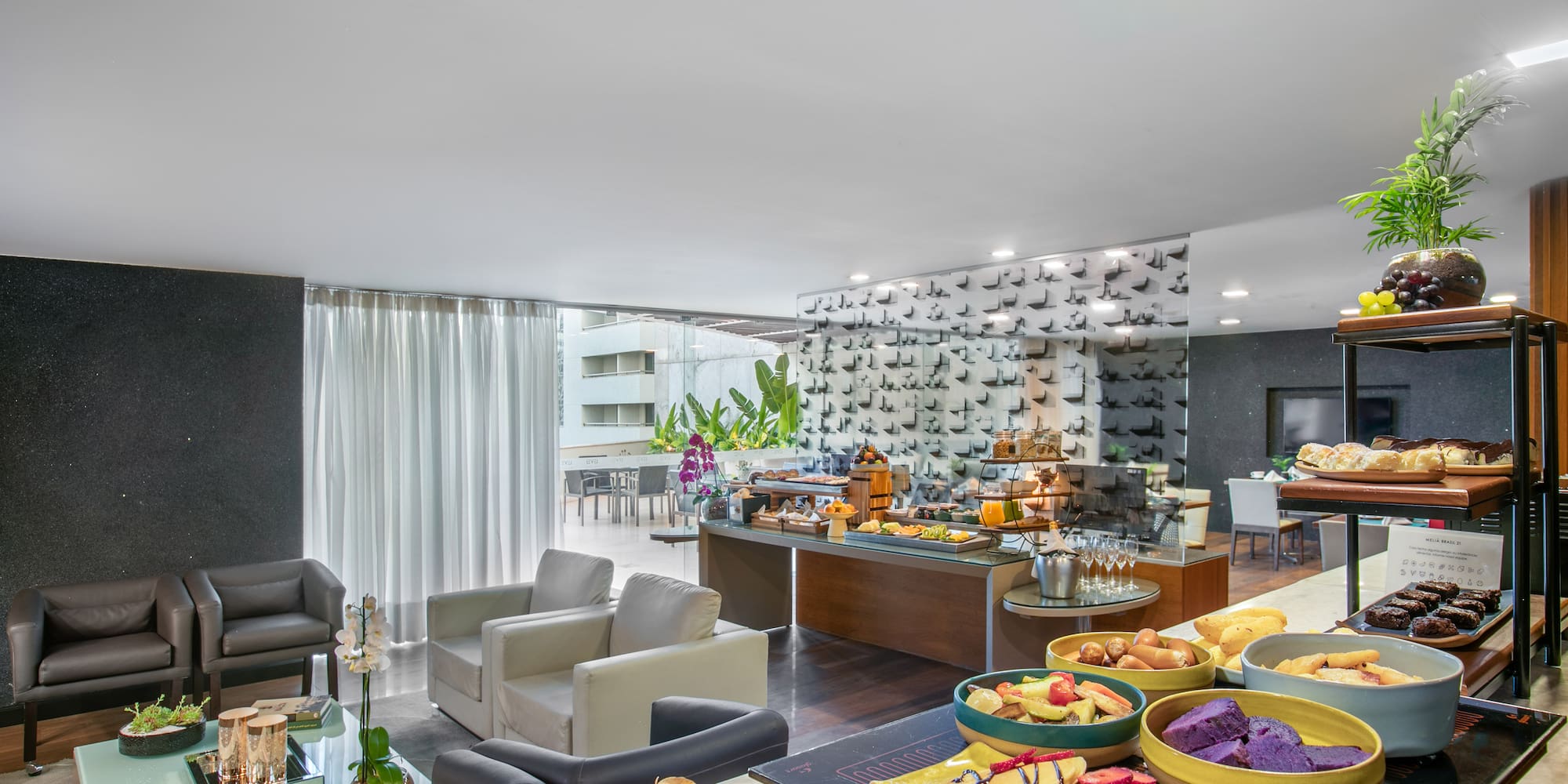 Hotel breakfast buffet with pastries, fruit, and lounge seating area.
