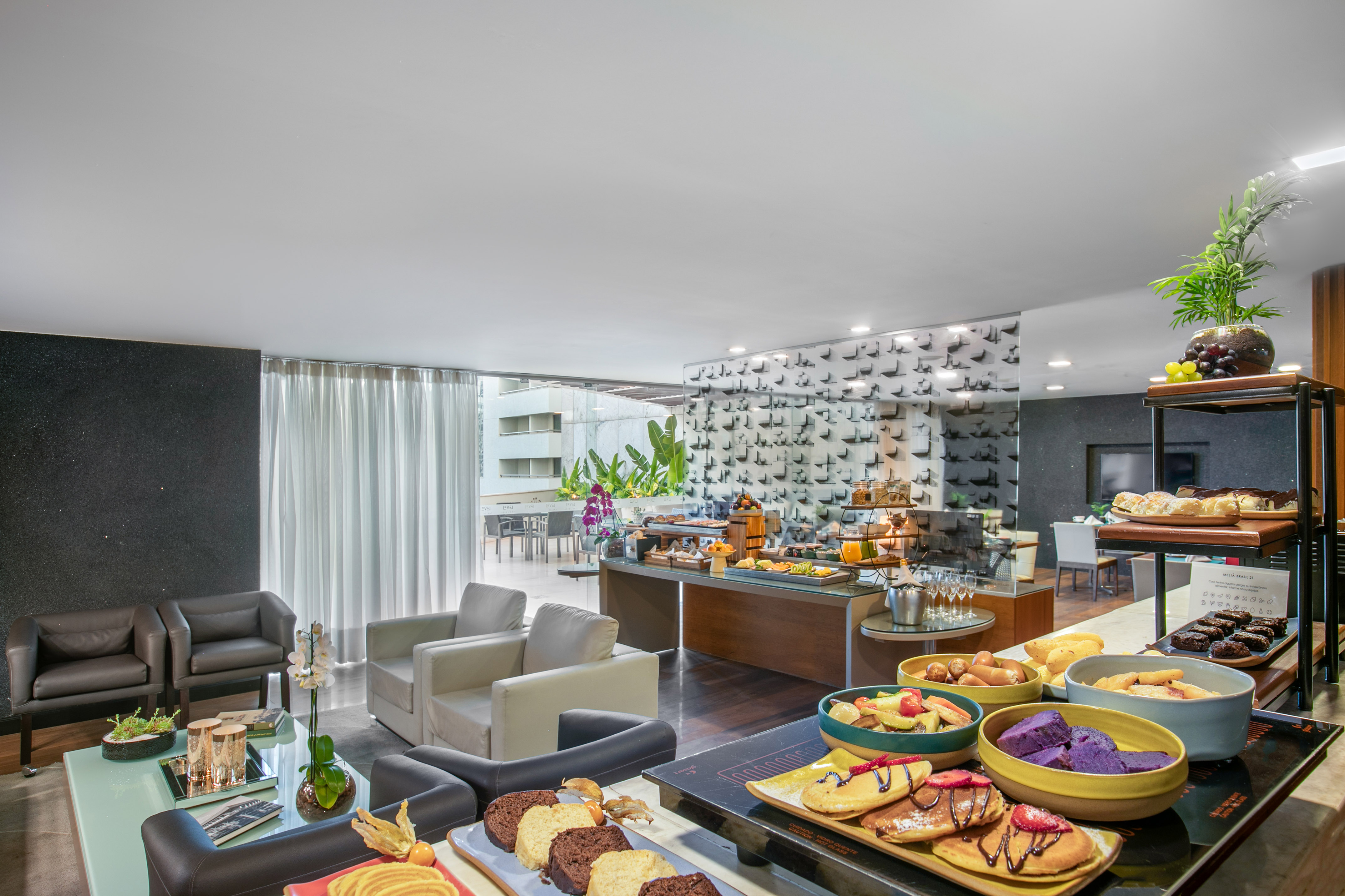 Hotel breakfast buffet with pastries, fruit, and lounge seating area.