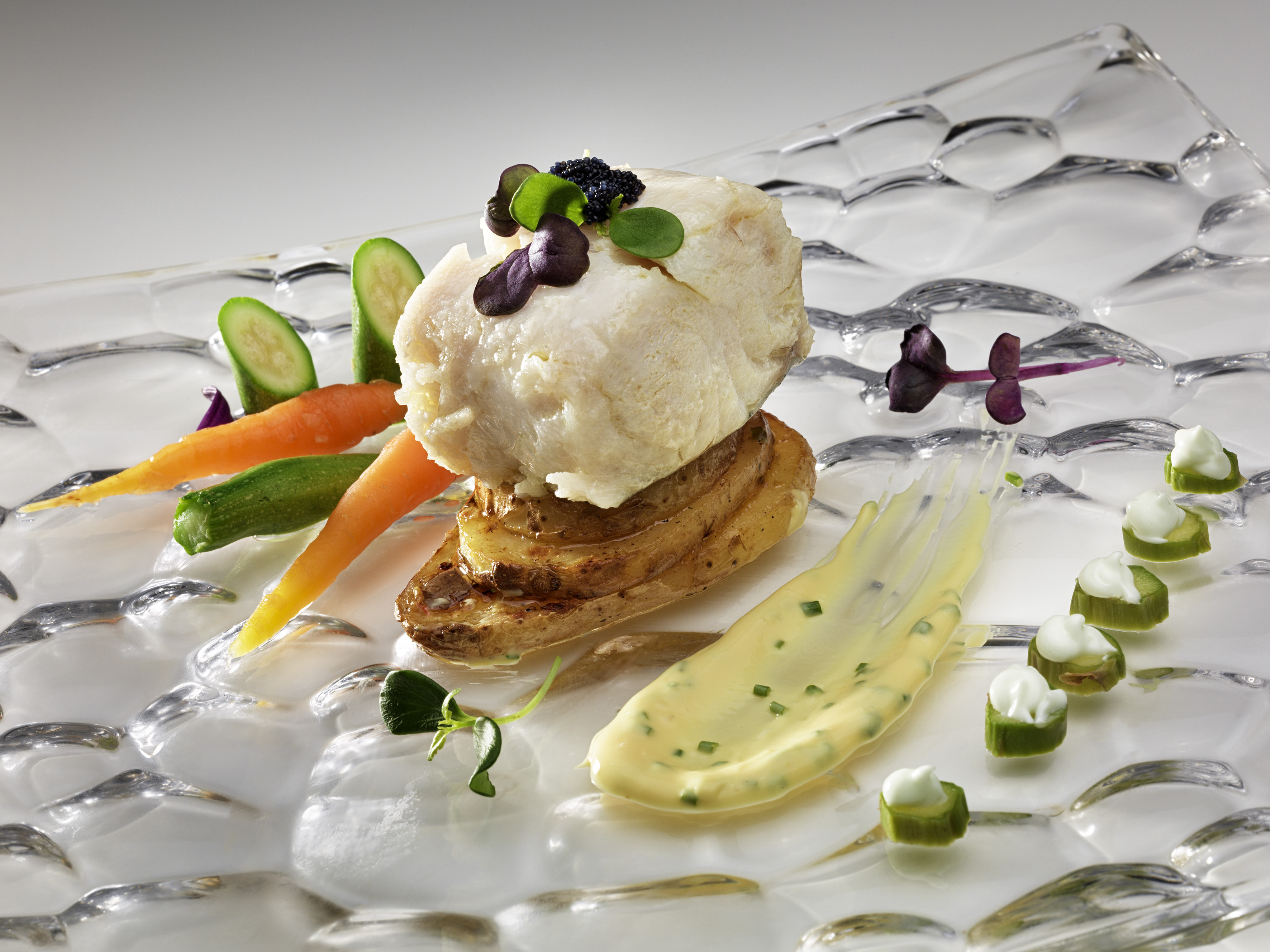 Gourmet white fish dish with caviar, potato, carrots, zucchini, and sauce.
