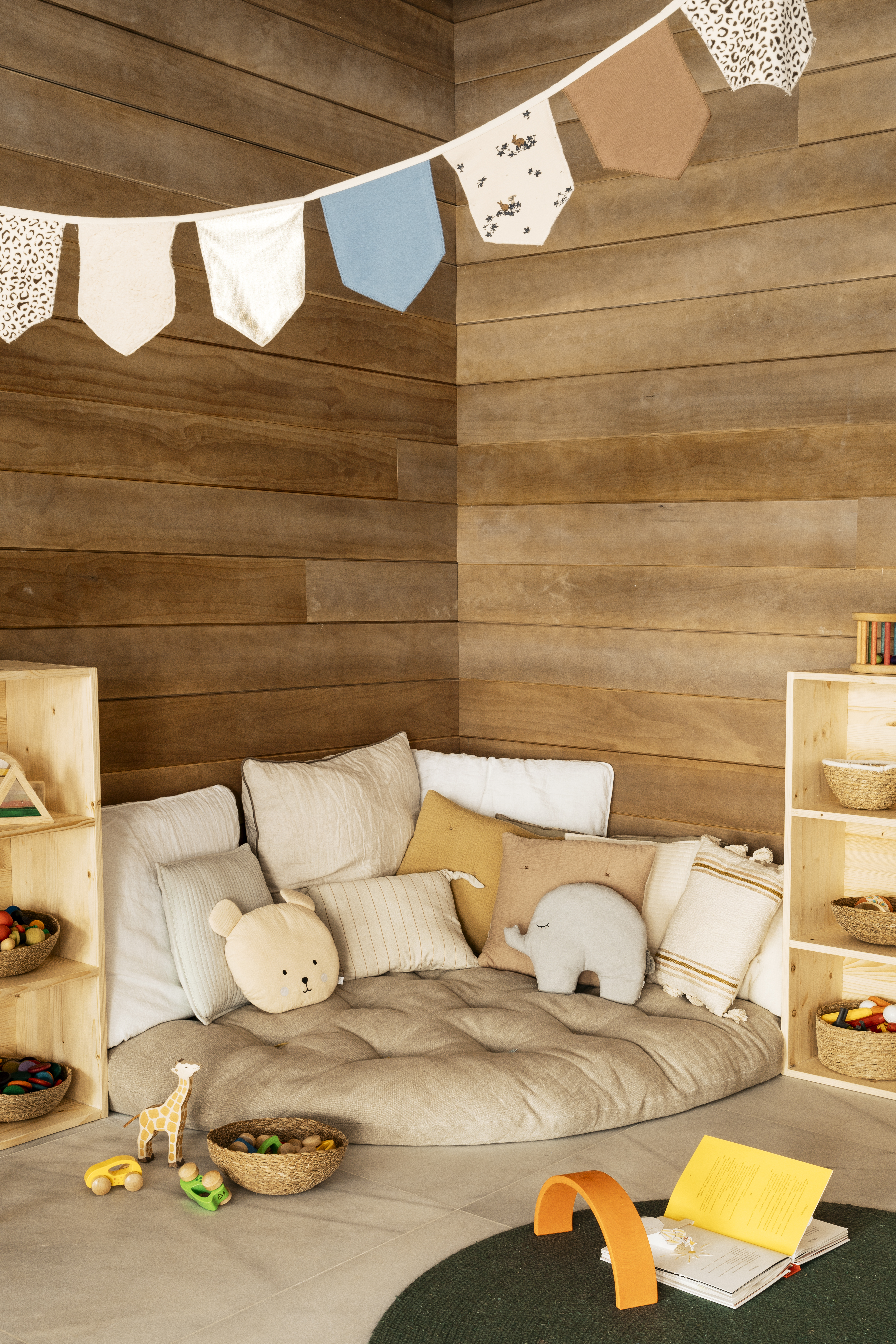 Cozy kids' corner: wood paneling, floor cushion, animal pillows, Montessori toys.