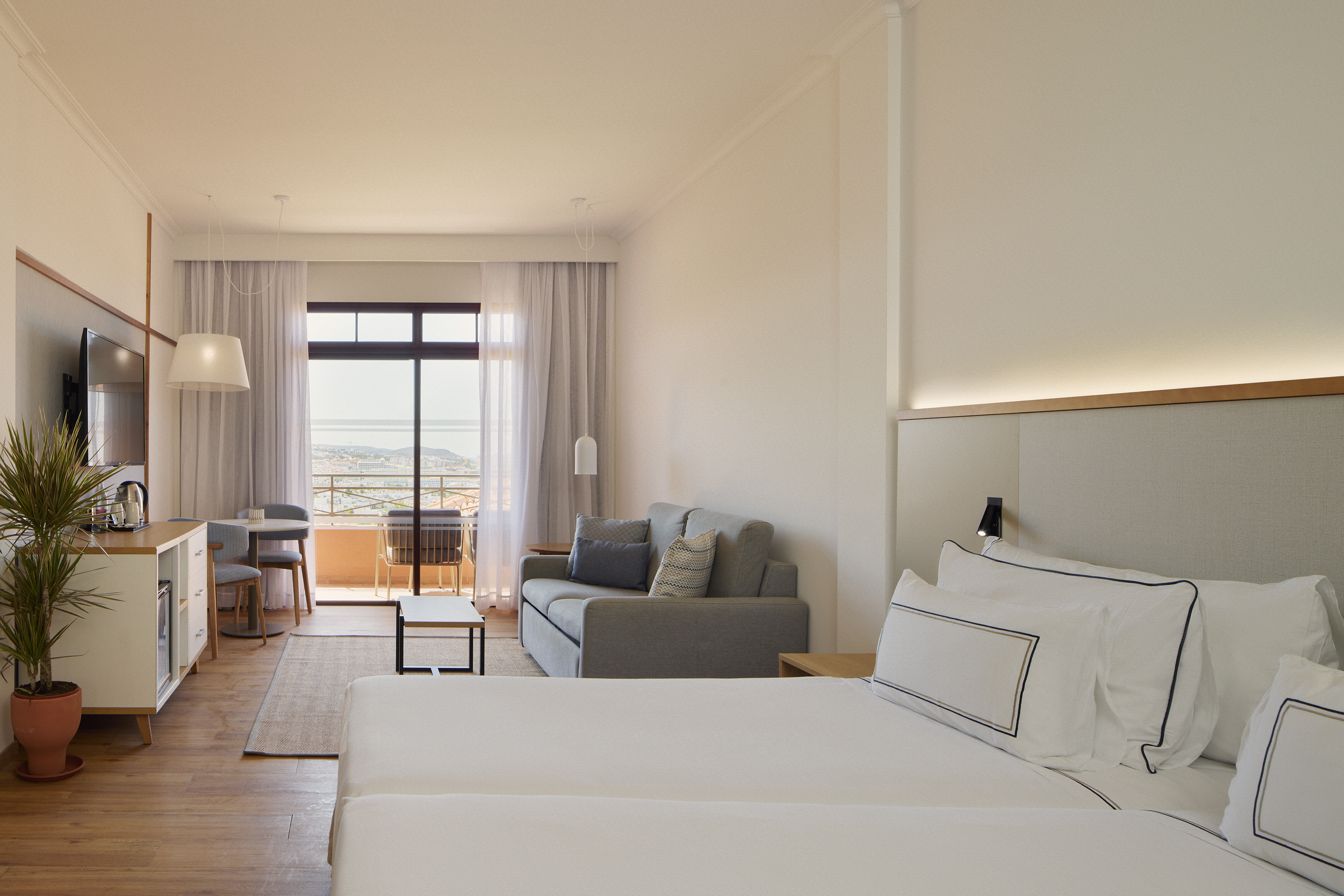 Spacious hotel suite with bed, sofa, balcony, and ocean city view.