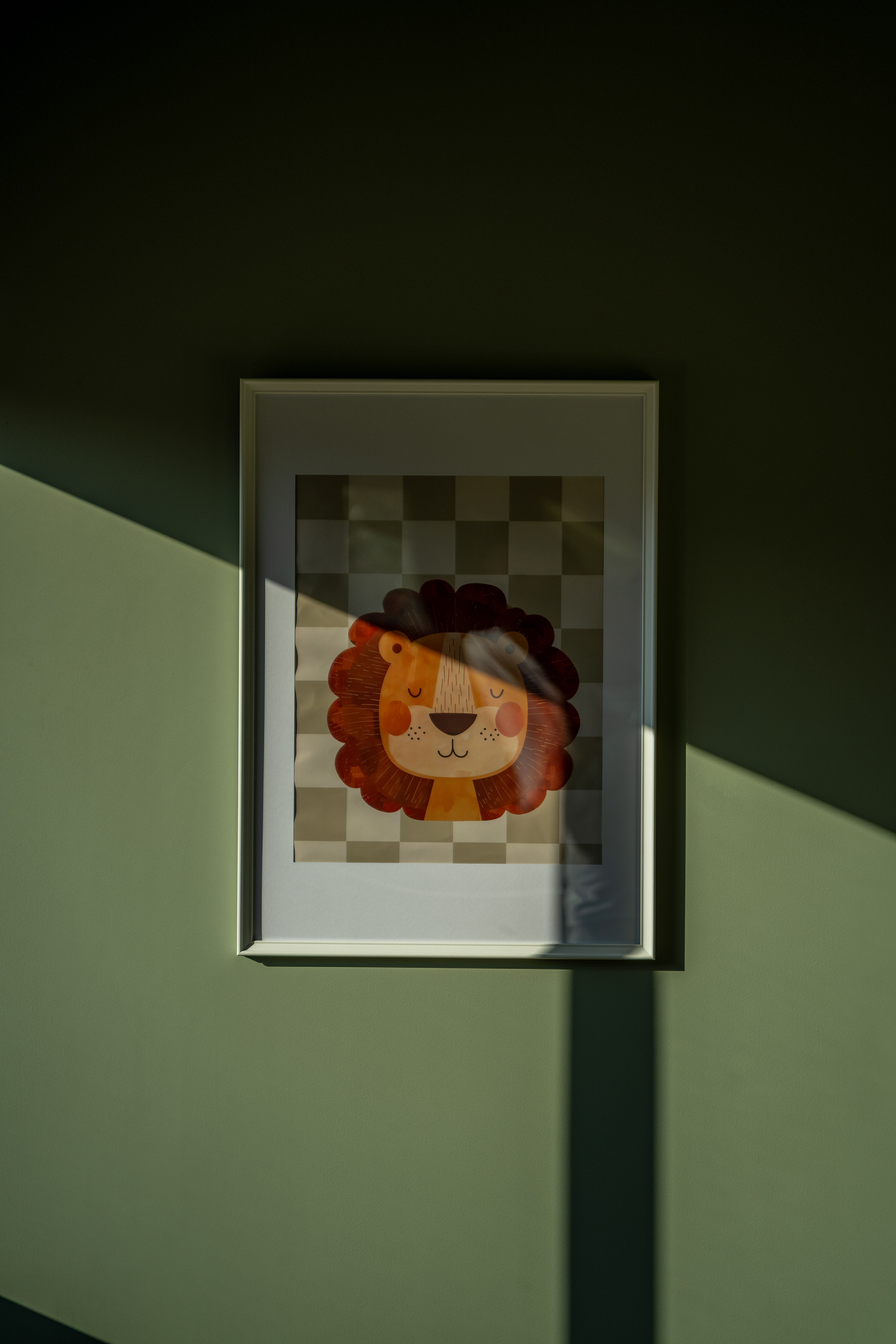 Framed cartoon lion print on green wall, sunlight and diagonal shadow.