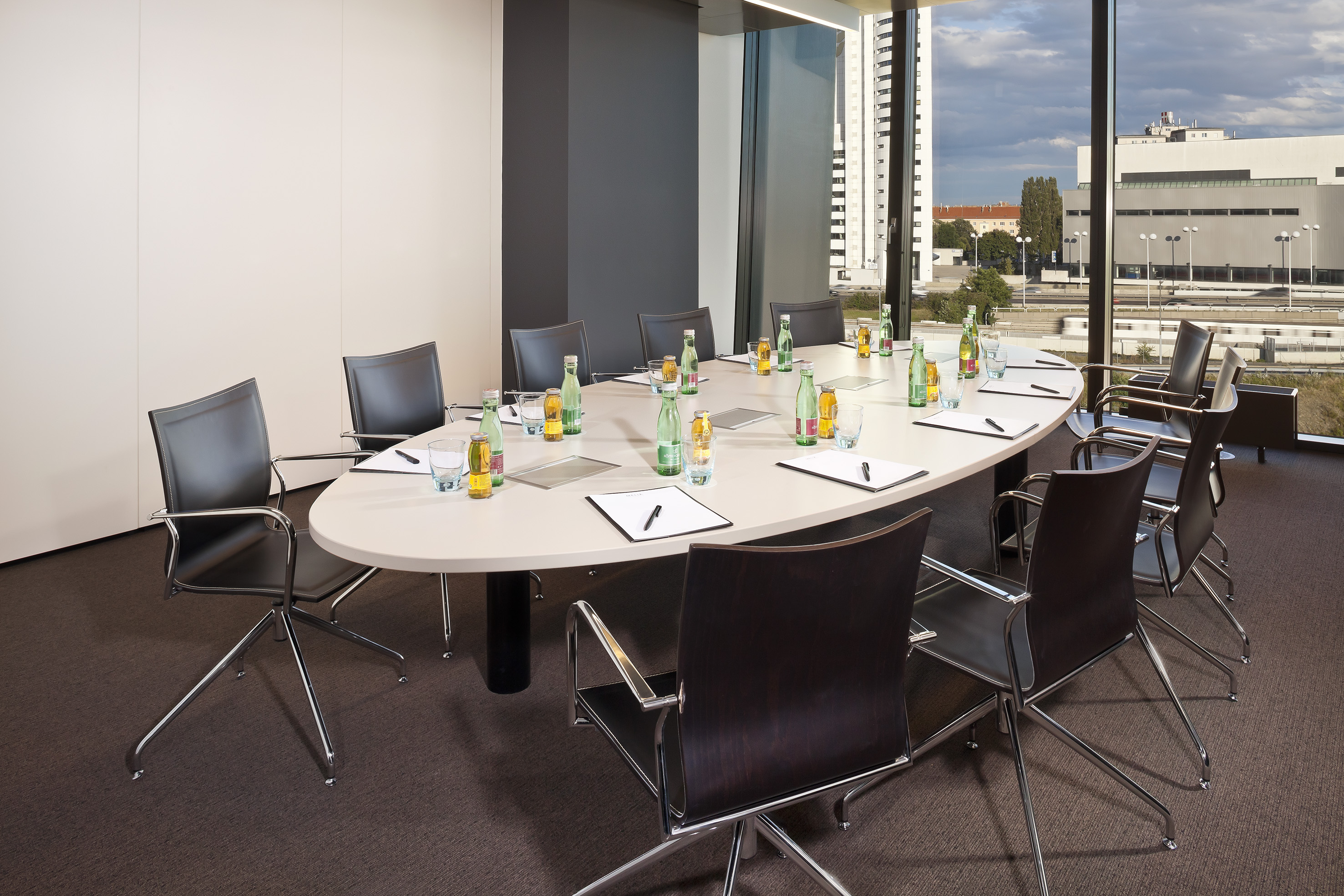 Modern conference room with oval table, chairs, water bottles, and city view.