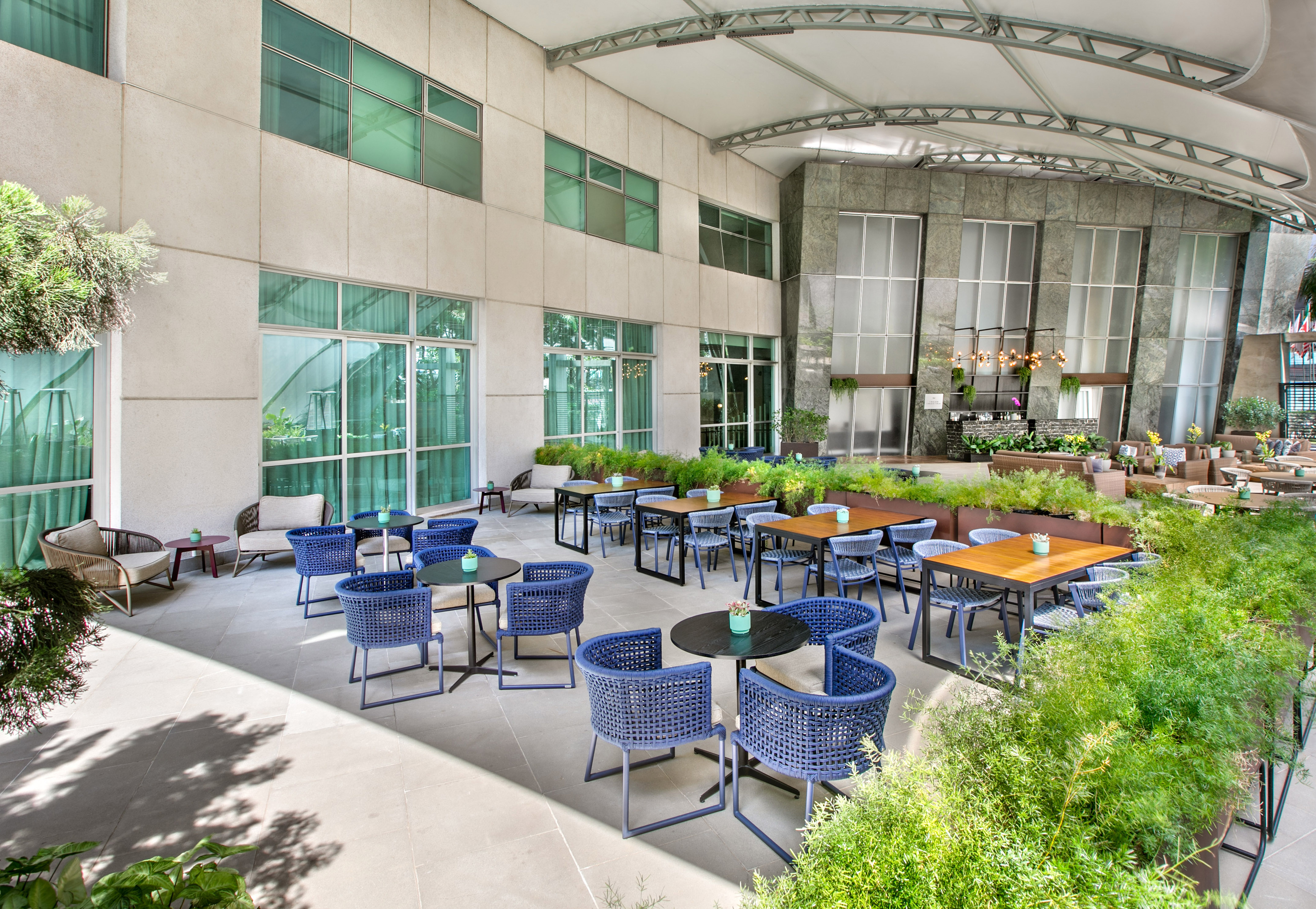 Modern outdoor hotel patio with blue seating and lush green plants.