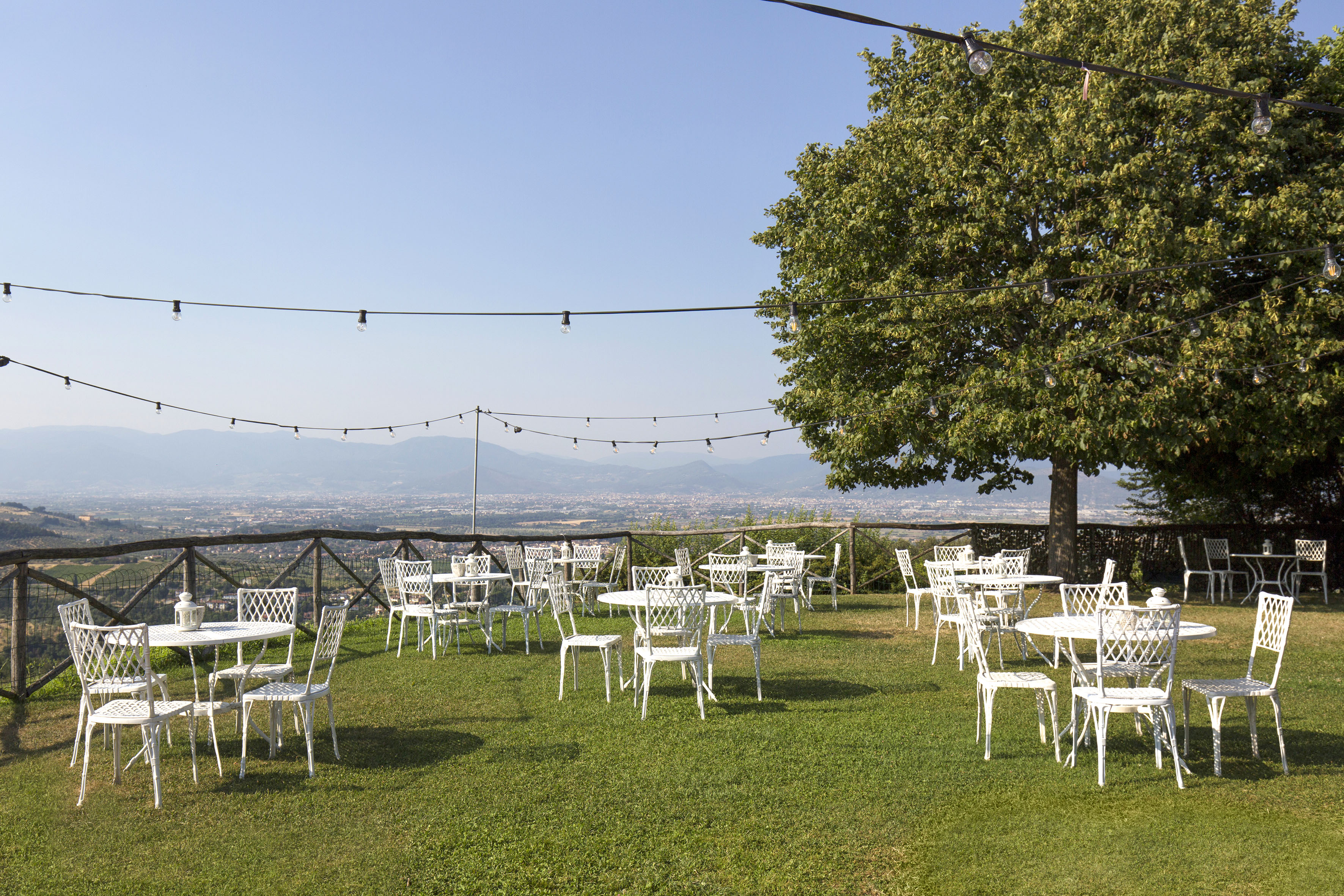 Outdoor dining terrace with white furniture, string lights, and valley view.