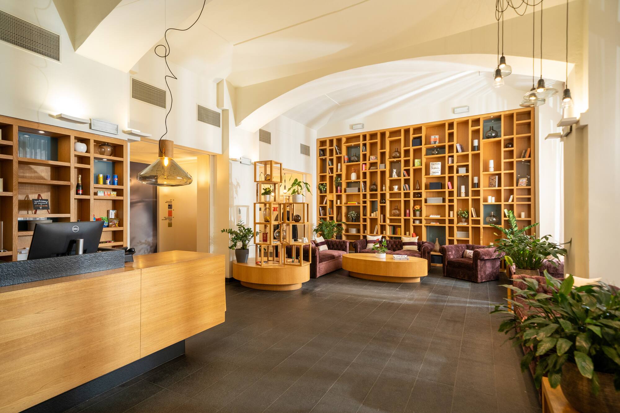 Modern hotel lobby with reception, wooden feature wall shelves, and seating.