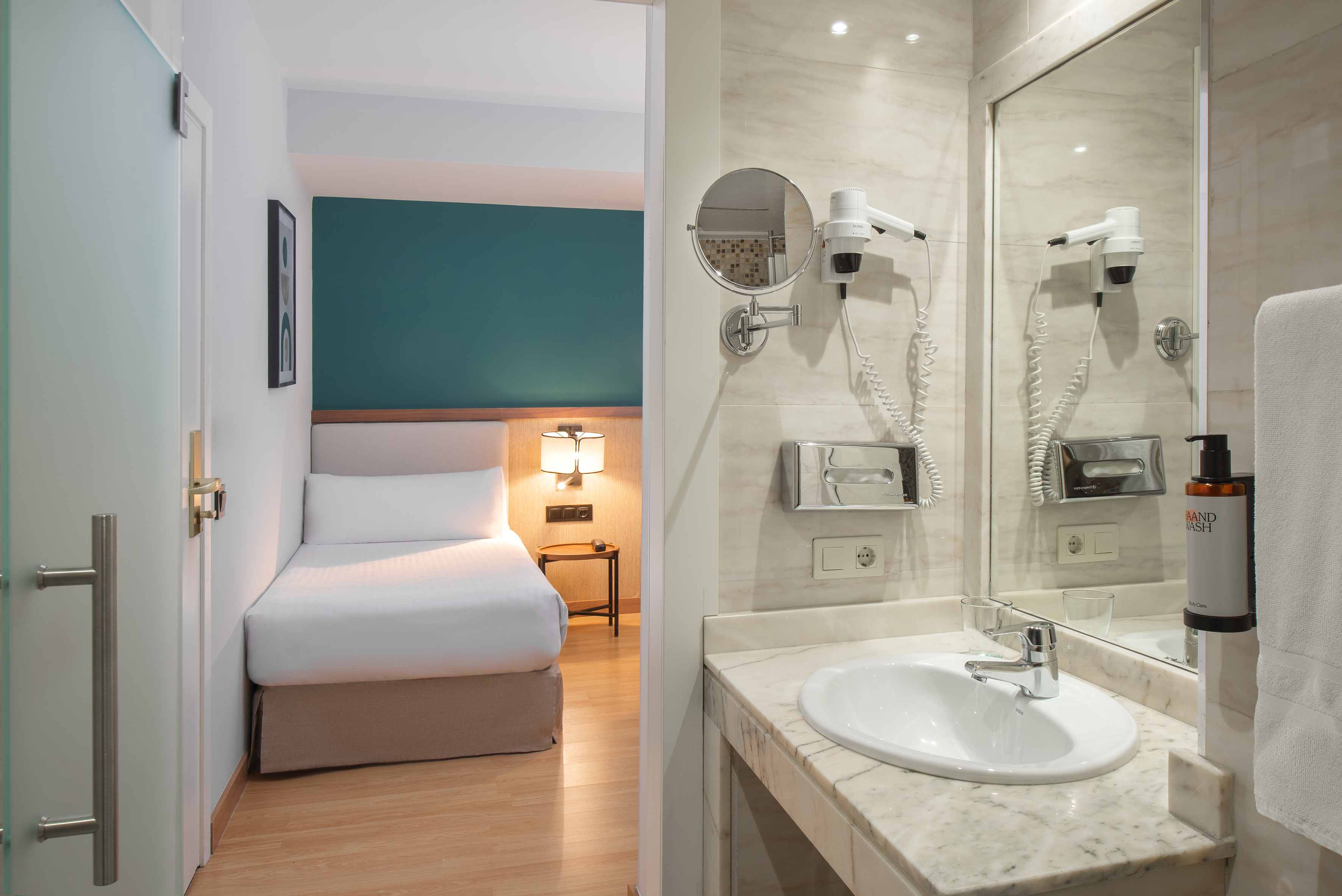Modern hotel room with single bed and bathroom featuring vanity, mirror.