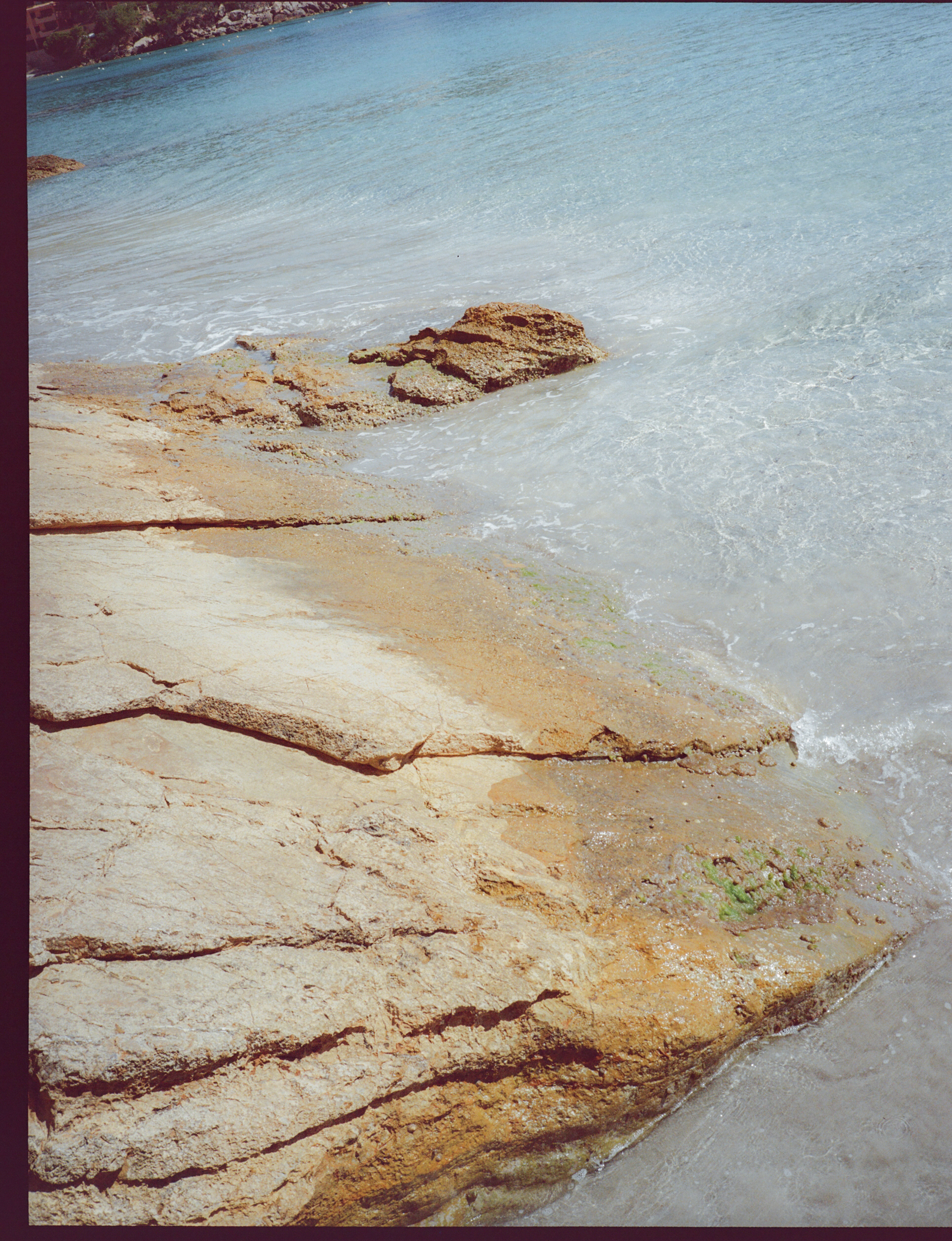 Clear turquoise water gently washing a rocky shoreline with brown and tan rocks.