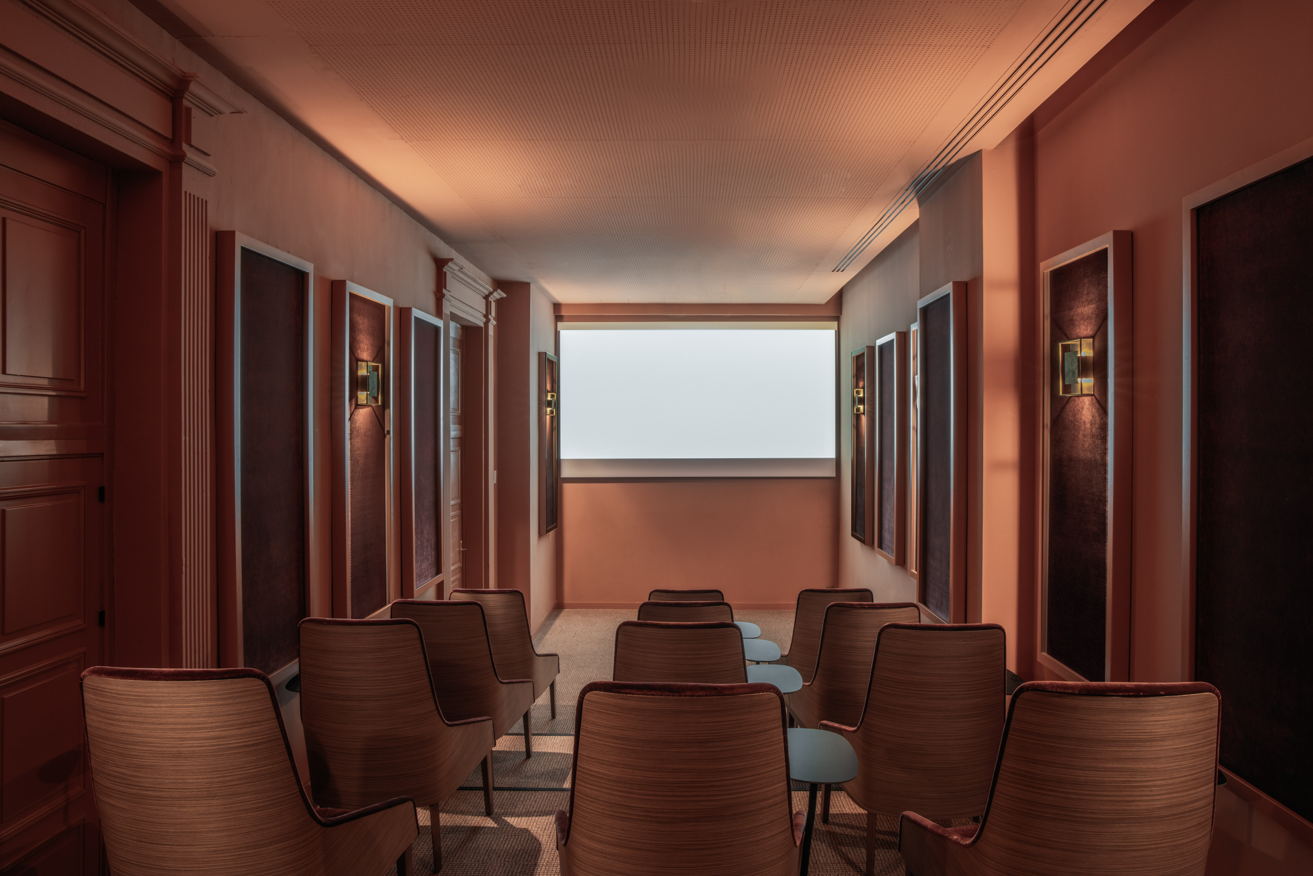 Warm, modern private cinema with wood chairs, large screen, and acoustic wall panels.