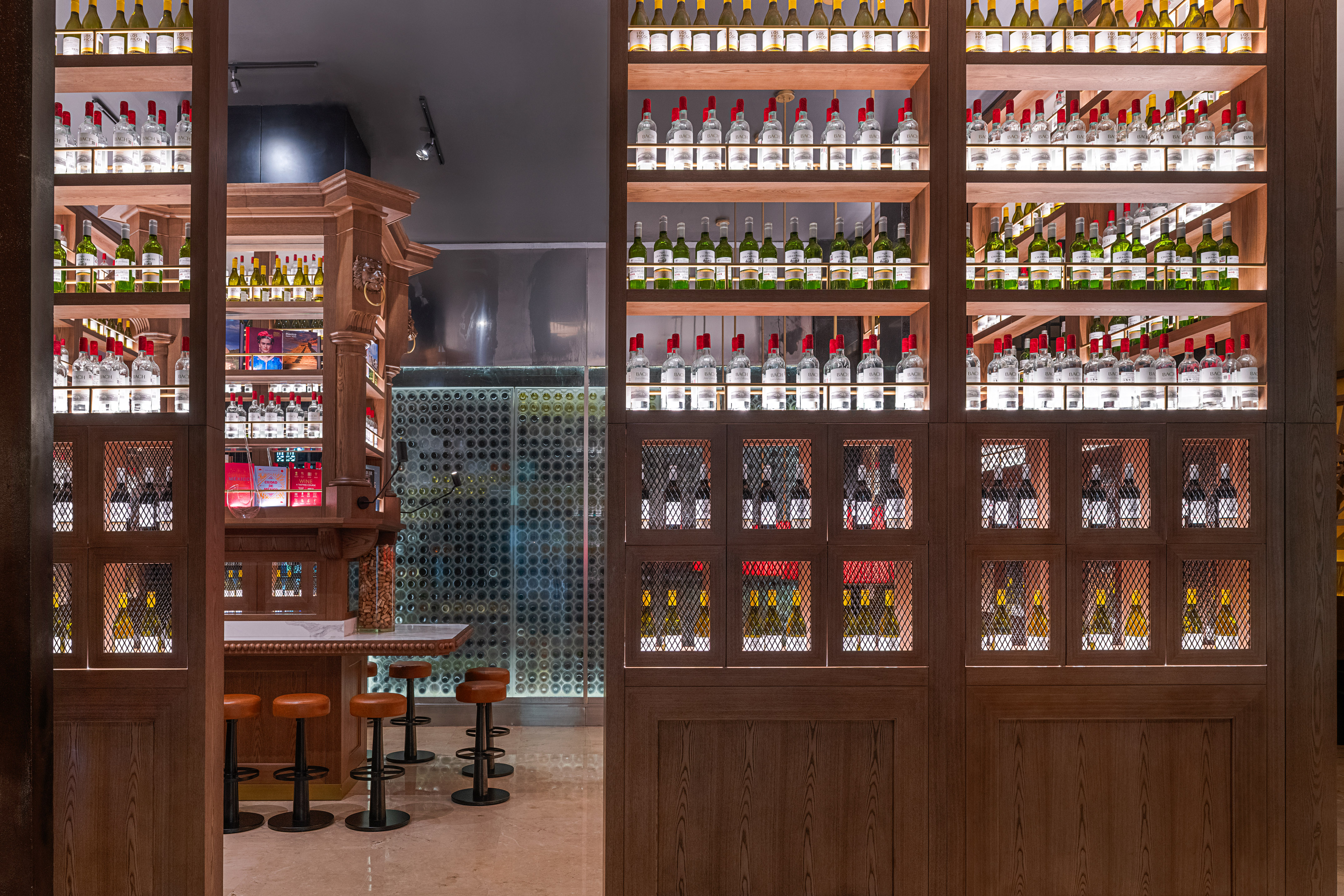 Illuminated liquor and wine bottle display on modern wooden bar shelves.