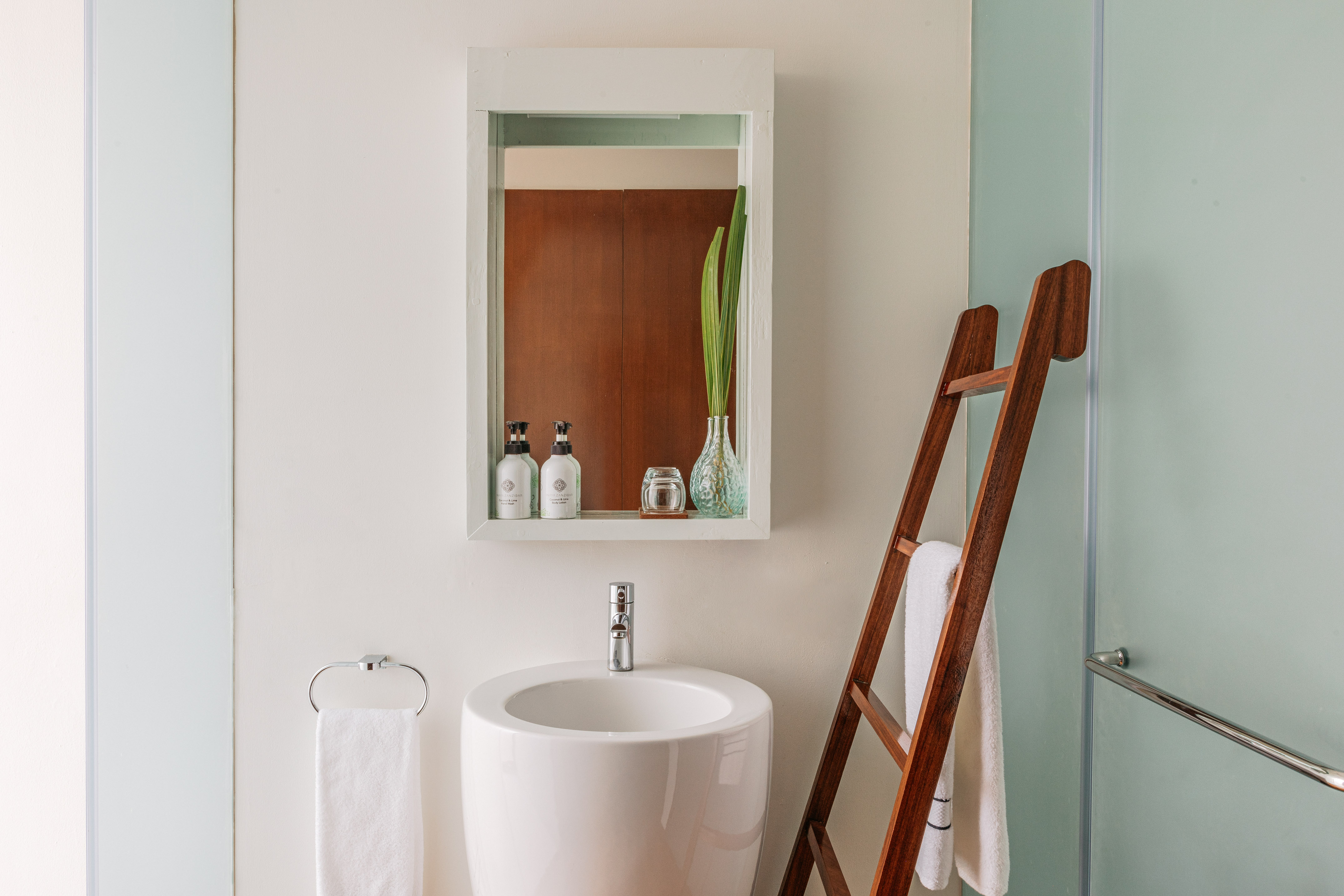 Modern bathroom with white sink, mirror, and wooden ladder towel rack.