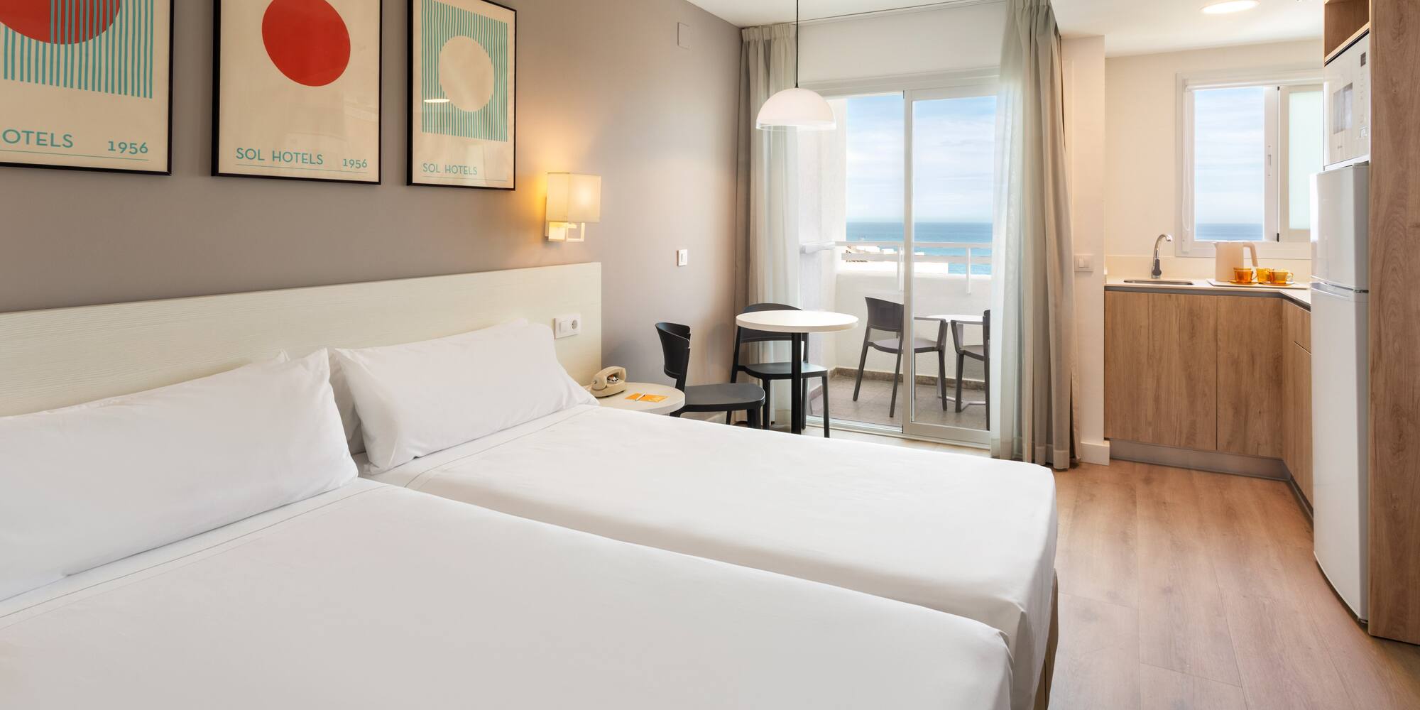 Hotel room with twin beds, kitchenette, and ocean view balcony.