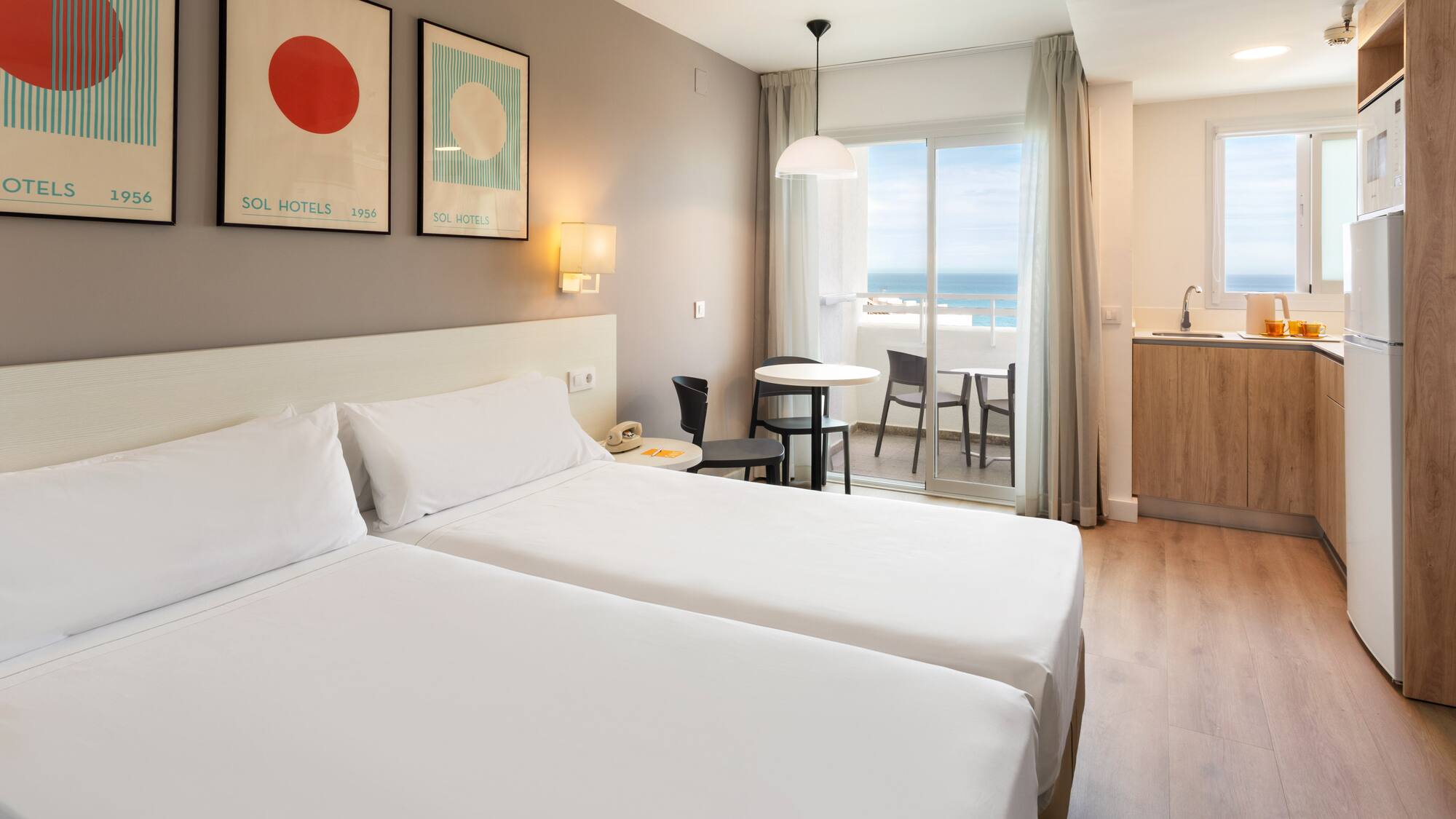 Hotel room with twin beds, kitchenette, and ocean view balcony.