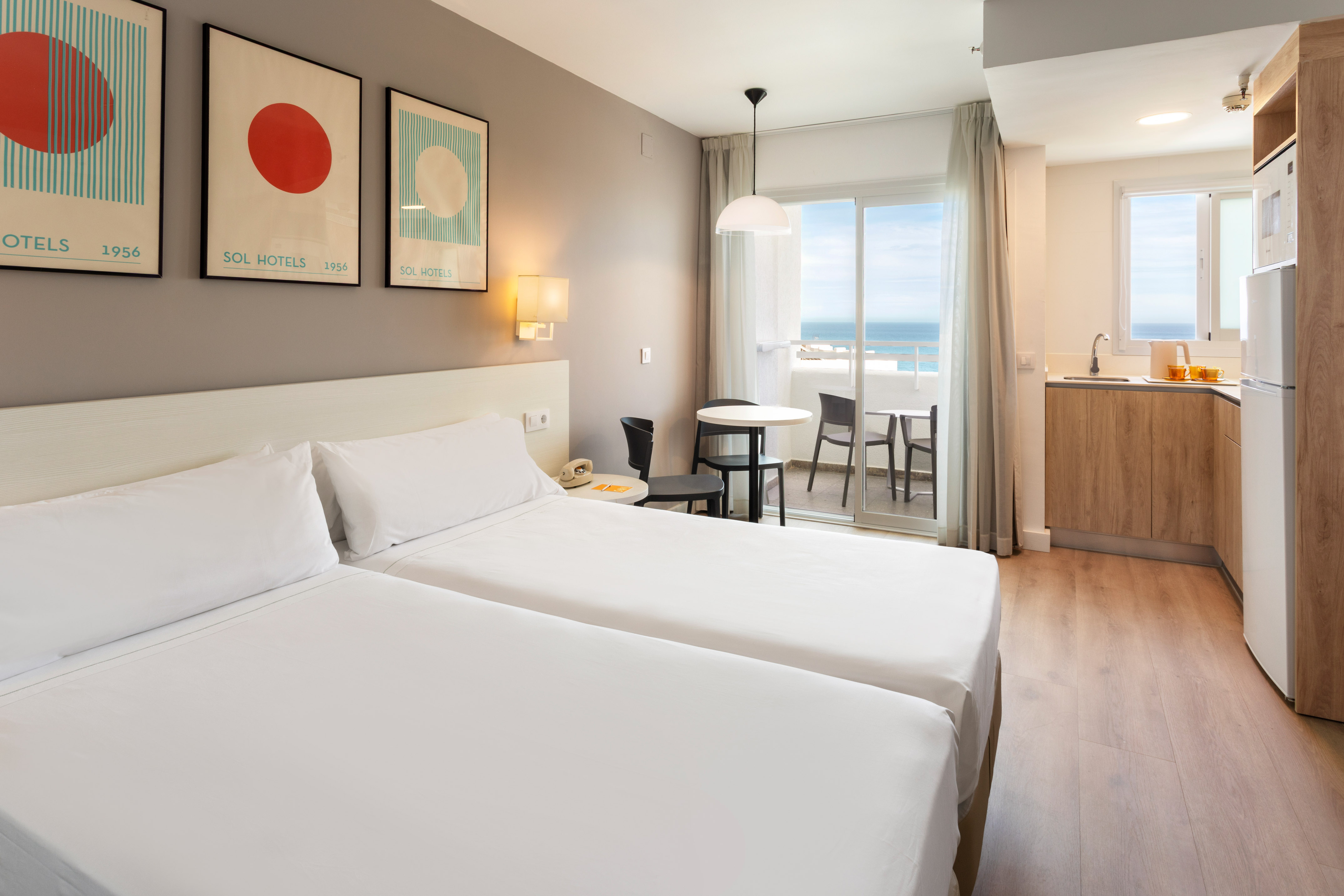 Modern hotel studio apartment with twin beds, kitchenette, and ocean view balcony.
