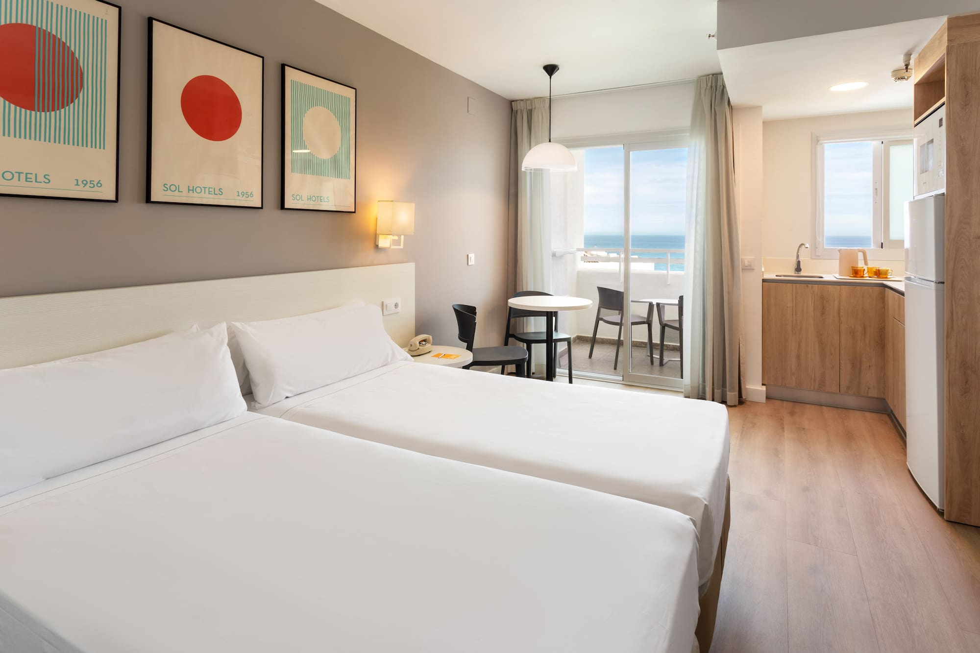 Modern hotel studio apartment with twin beds, kitchenette, and ocean view balcony.