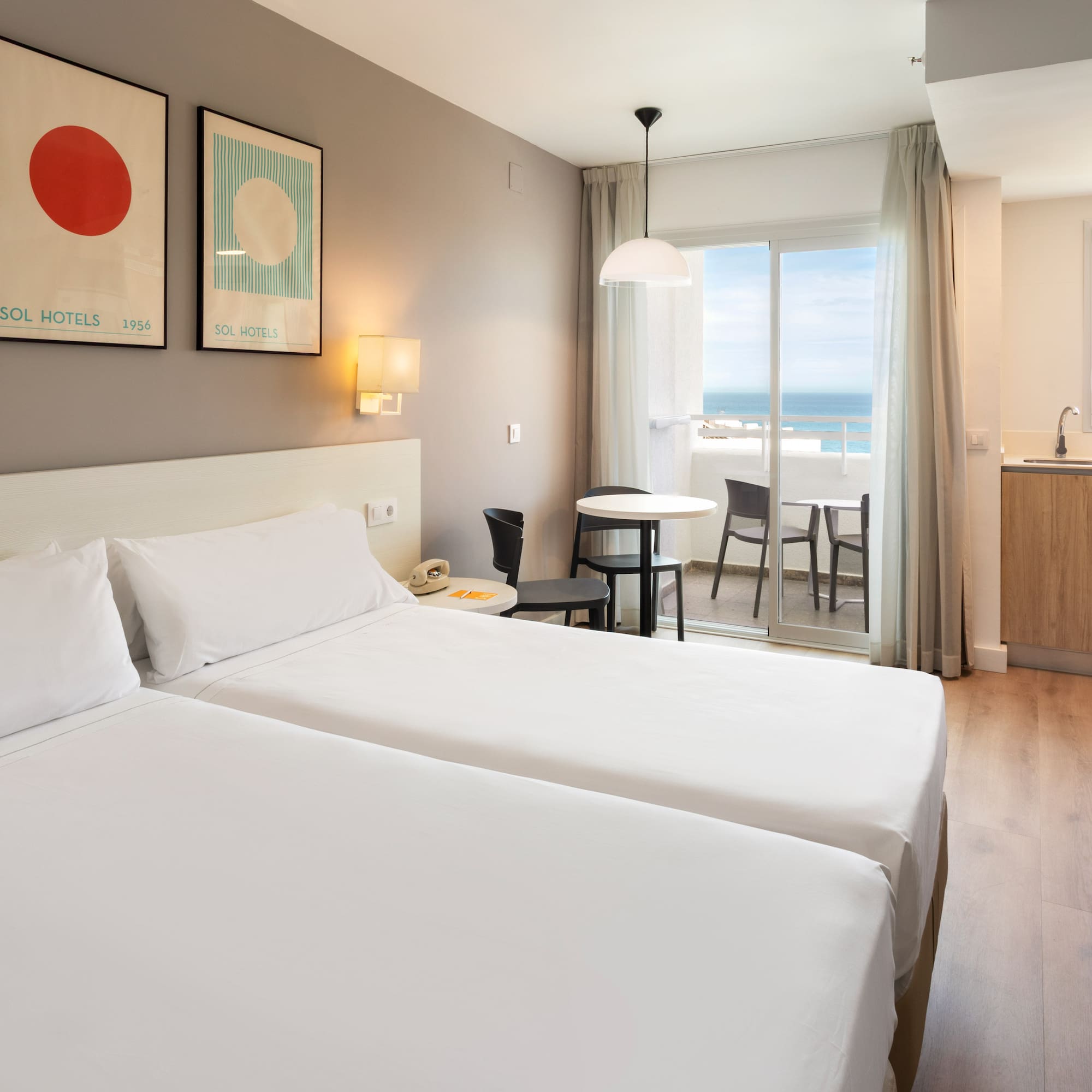 Hotel room with twin beds, kitchenette, and ocean view balcony.