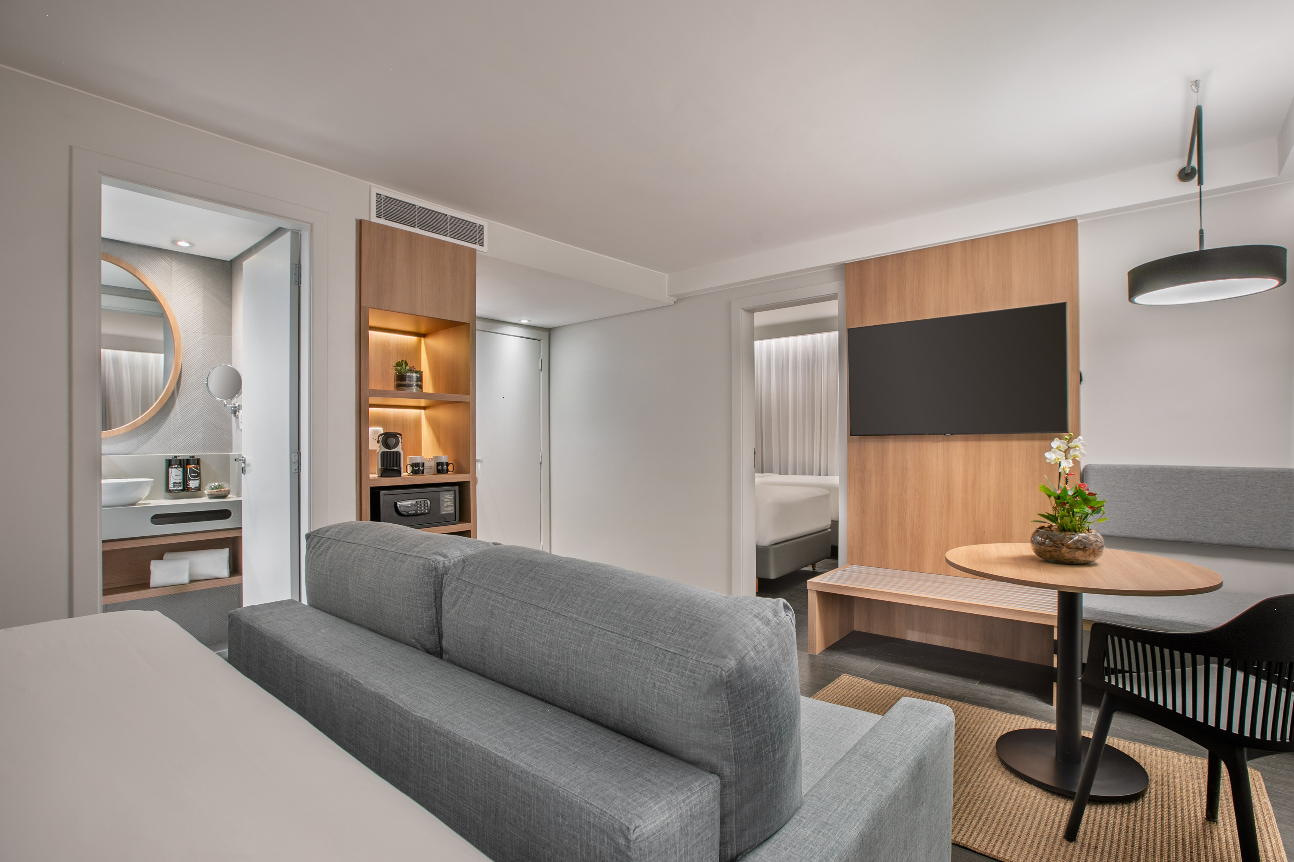Modern hotel suite living area with sofa, TV, and contemporary bathroom.