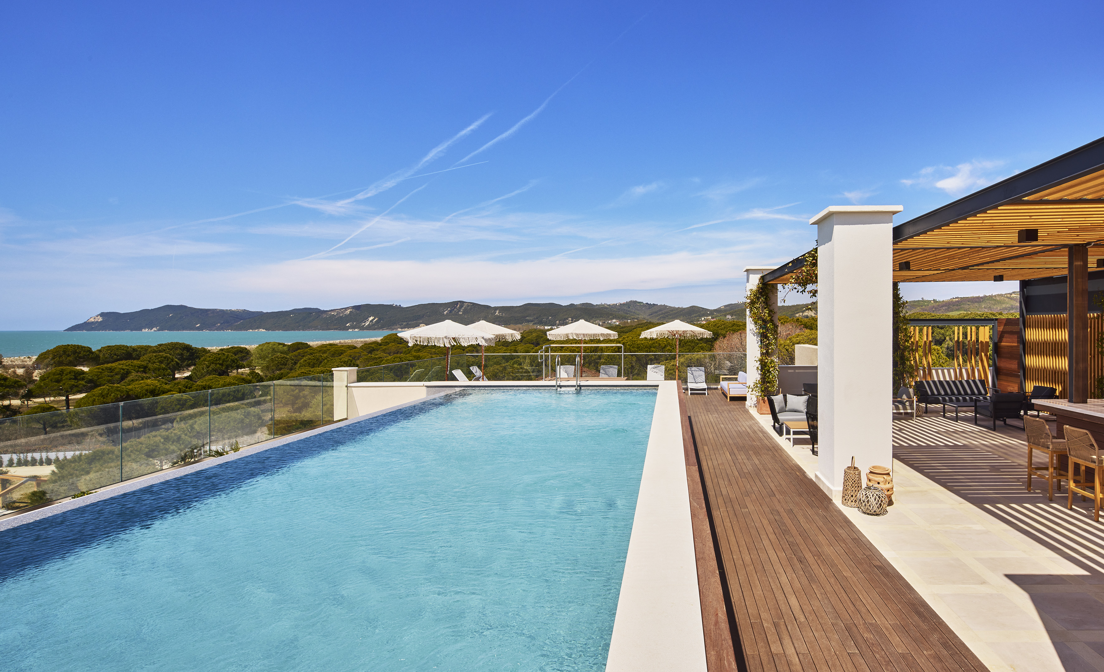 Ocean view infinity pool, sandy beach, green hills, and modern outdoor lounge area.