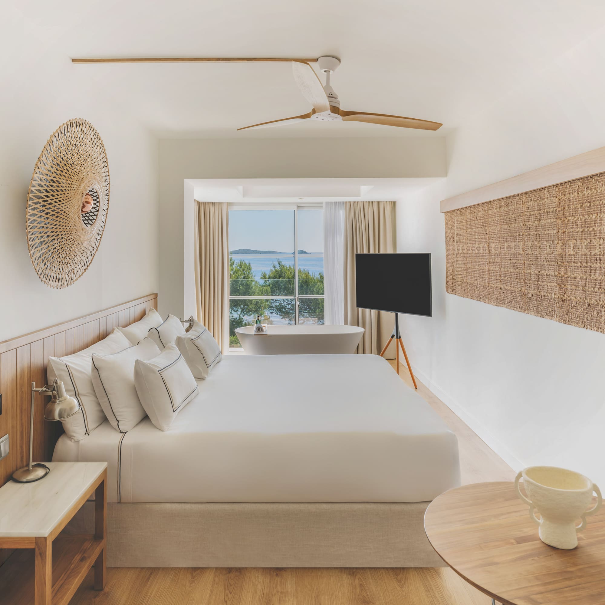 Modern hotel room with sea view, large bed, and freestanding bathtub.