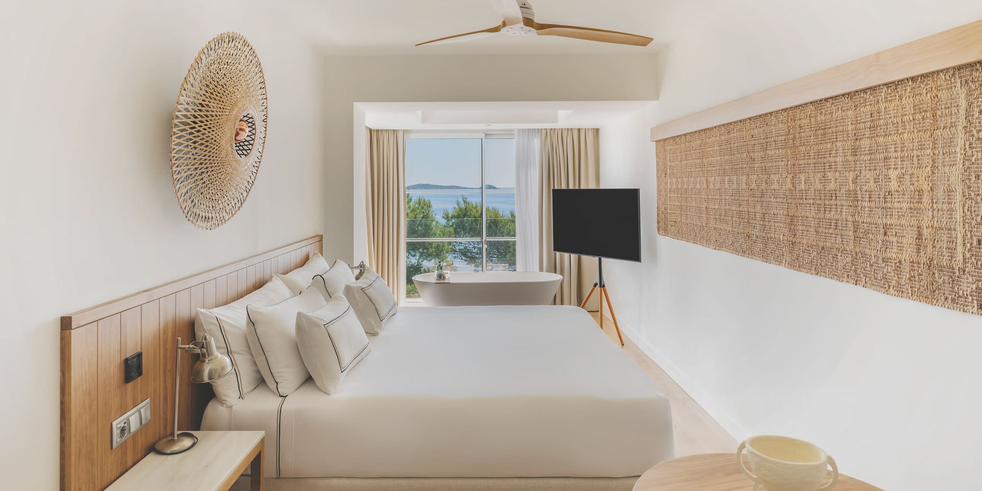 Modern hotel room with sea view, large bed, and freestanding bathtub.