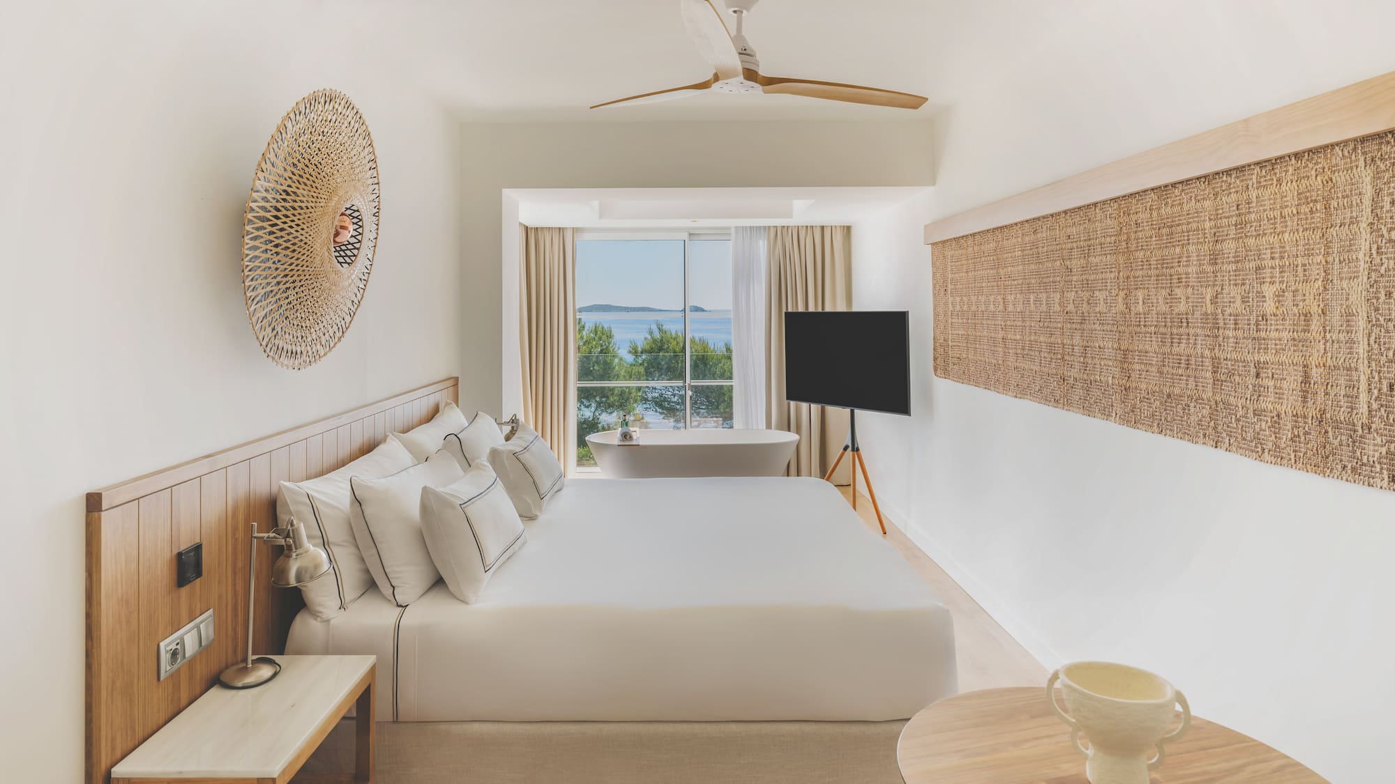 Modern hotel room with sea view, large bed, and freestanding bathtub.