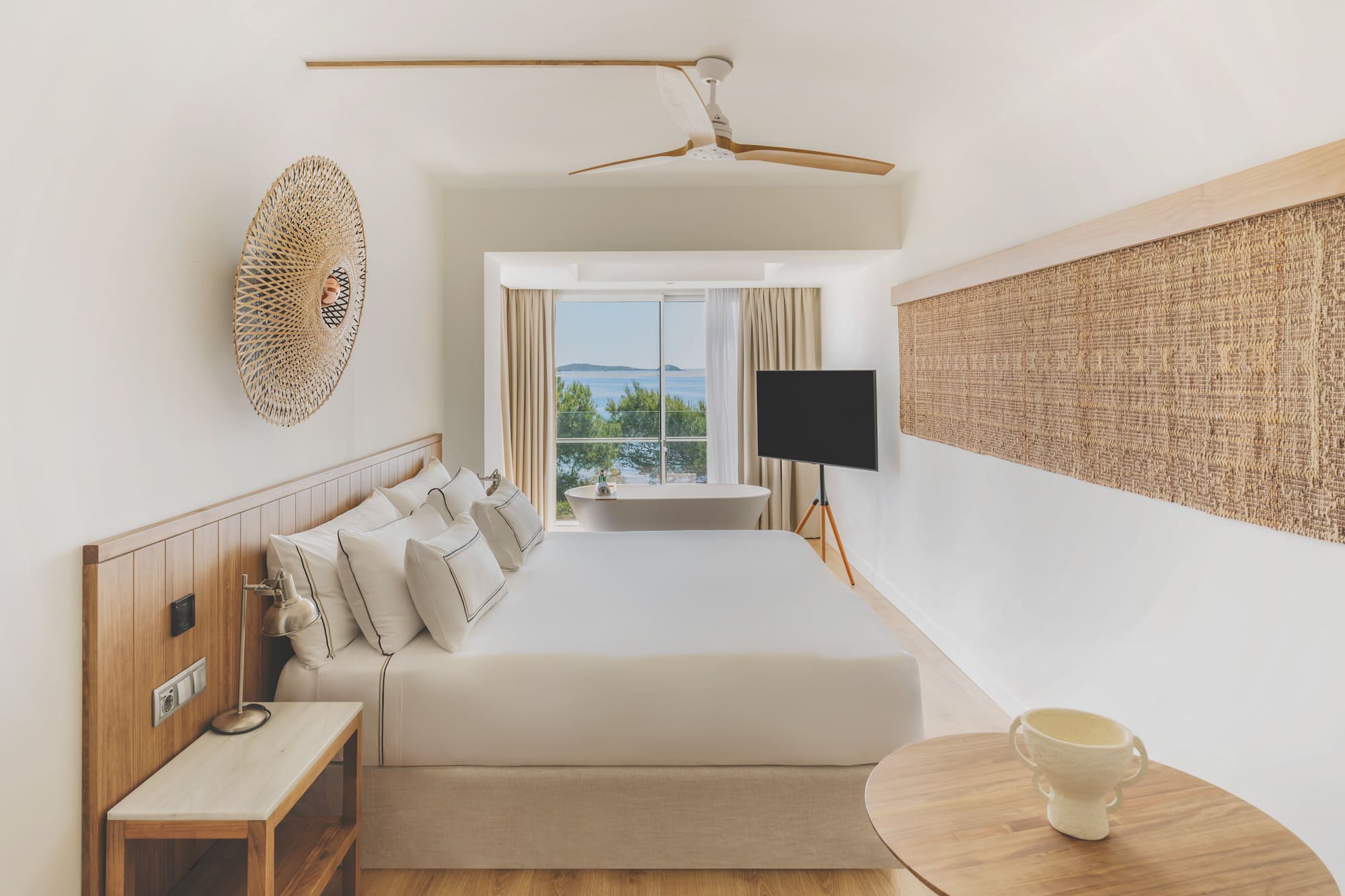 Modern hotel room with sea view, large bed, and freestanding bathtub.