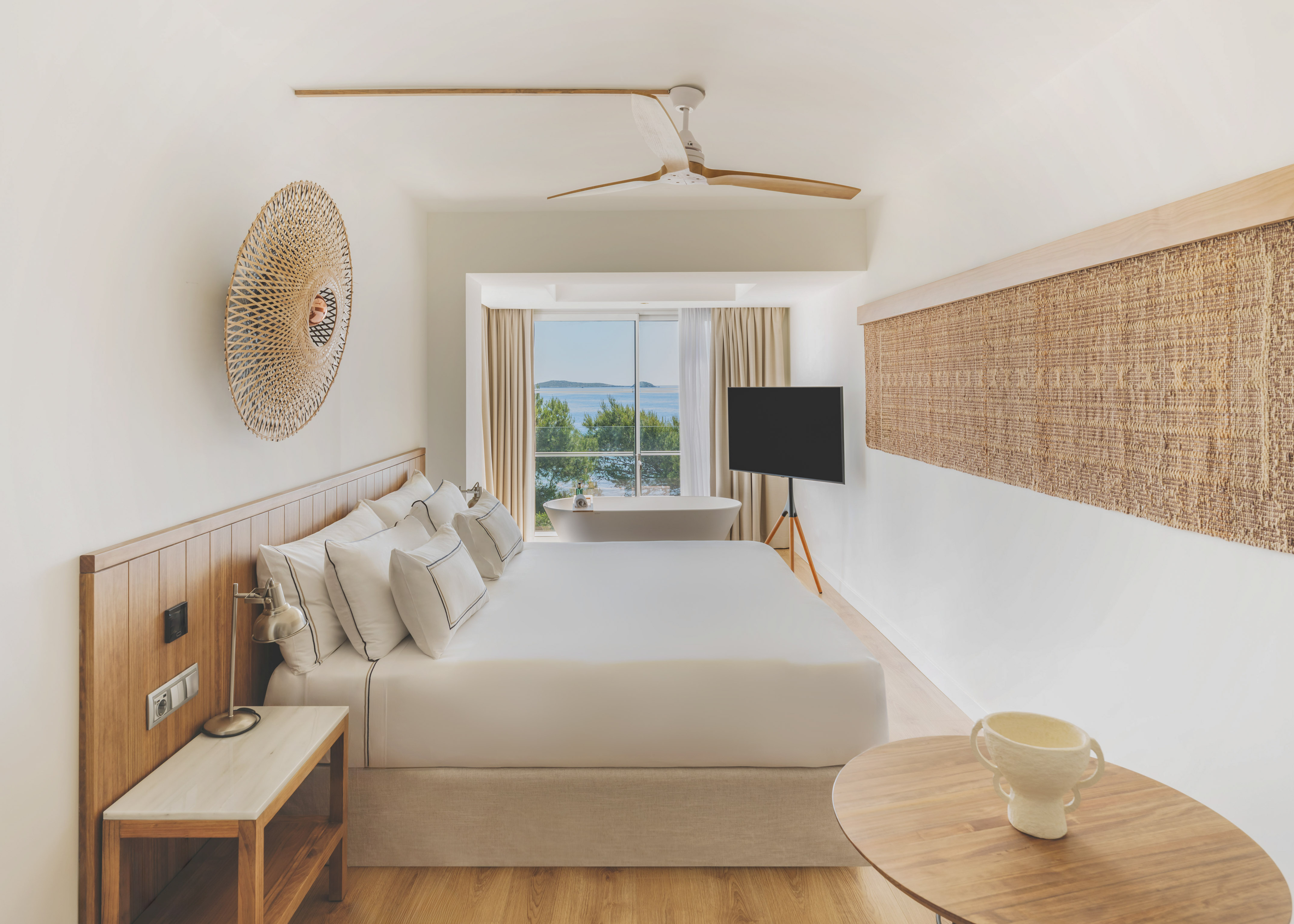 Modern hotel room with sea view, large bed, and freestanding bathtub.