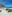 White sand beach, large palapa with bench, turquoise ocean, and blue sky.
