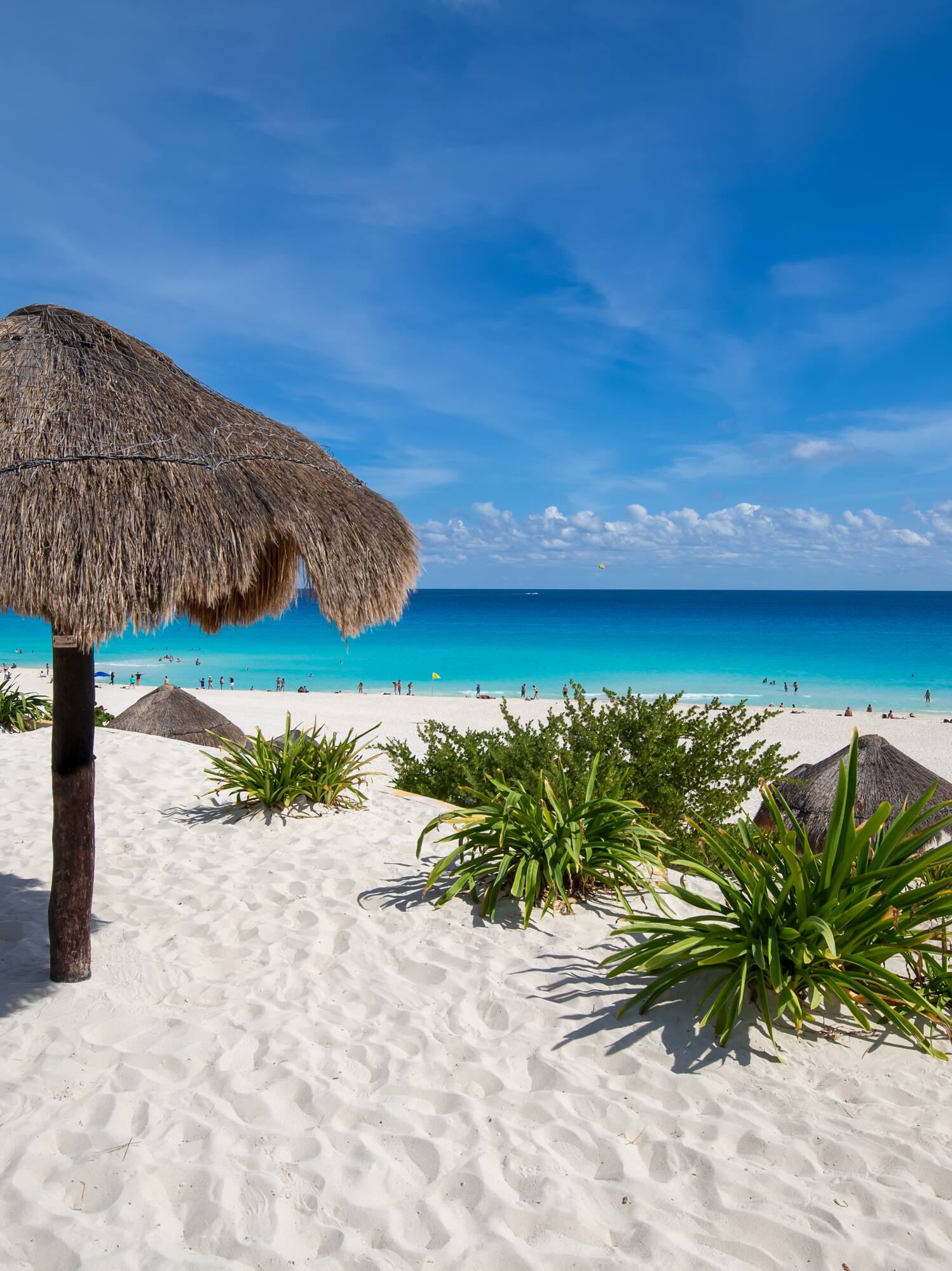 White sand beach, large palapa with bench, turquoise ocean, and blue sky.