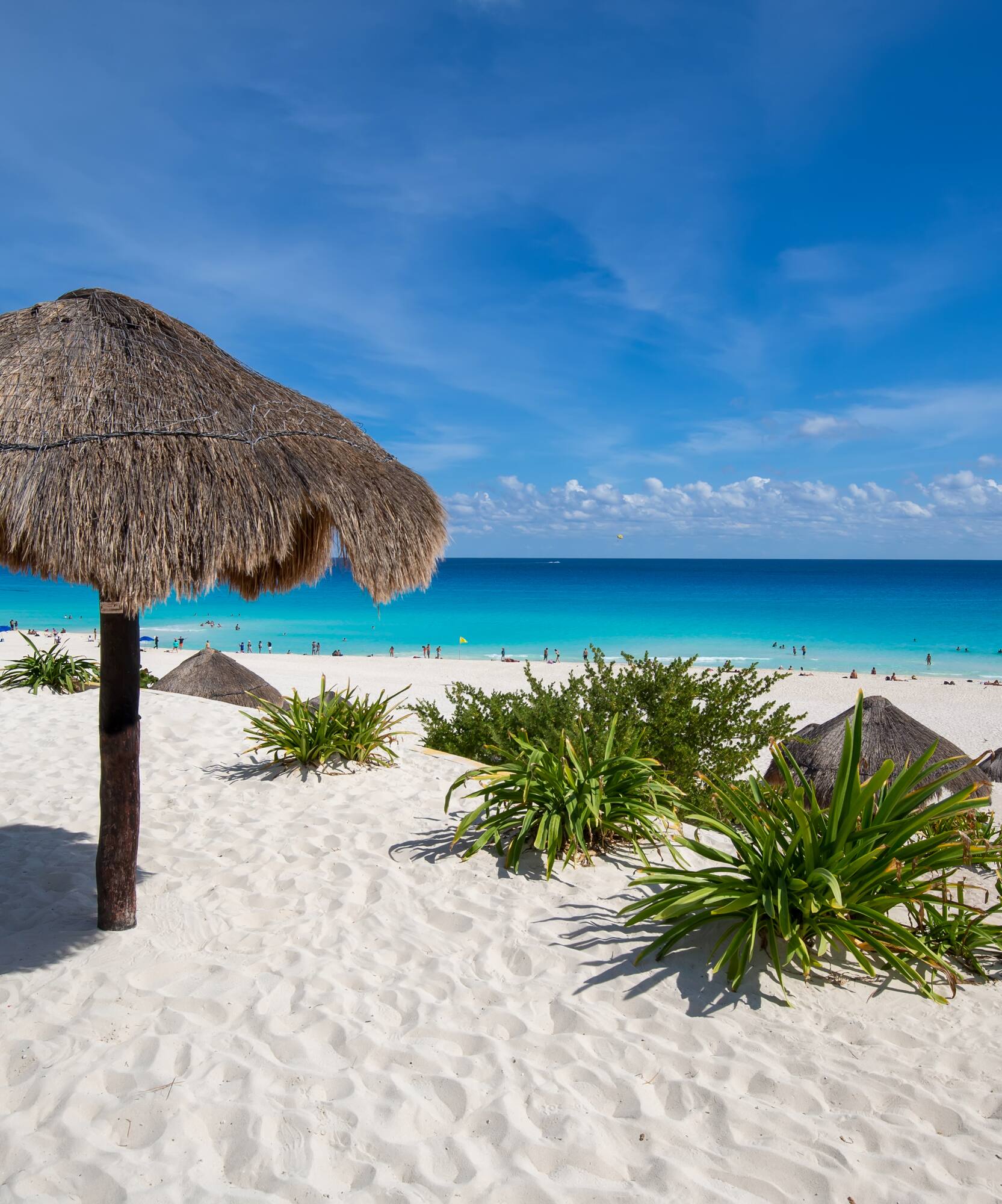 White sand beach, large palapa with bench, turquoise ocean, and blue sky.