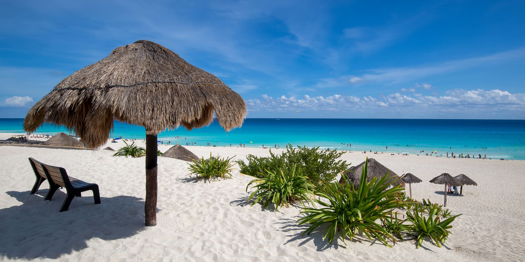Playa tropical con arena blanca, mar turquesa y palapa.