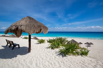 a beach with a straw umbrella and a chair