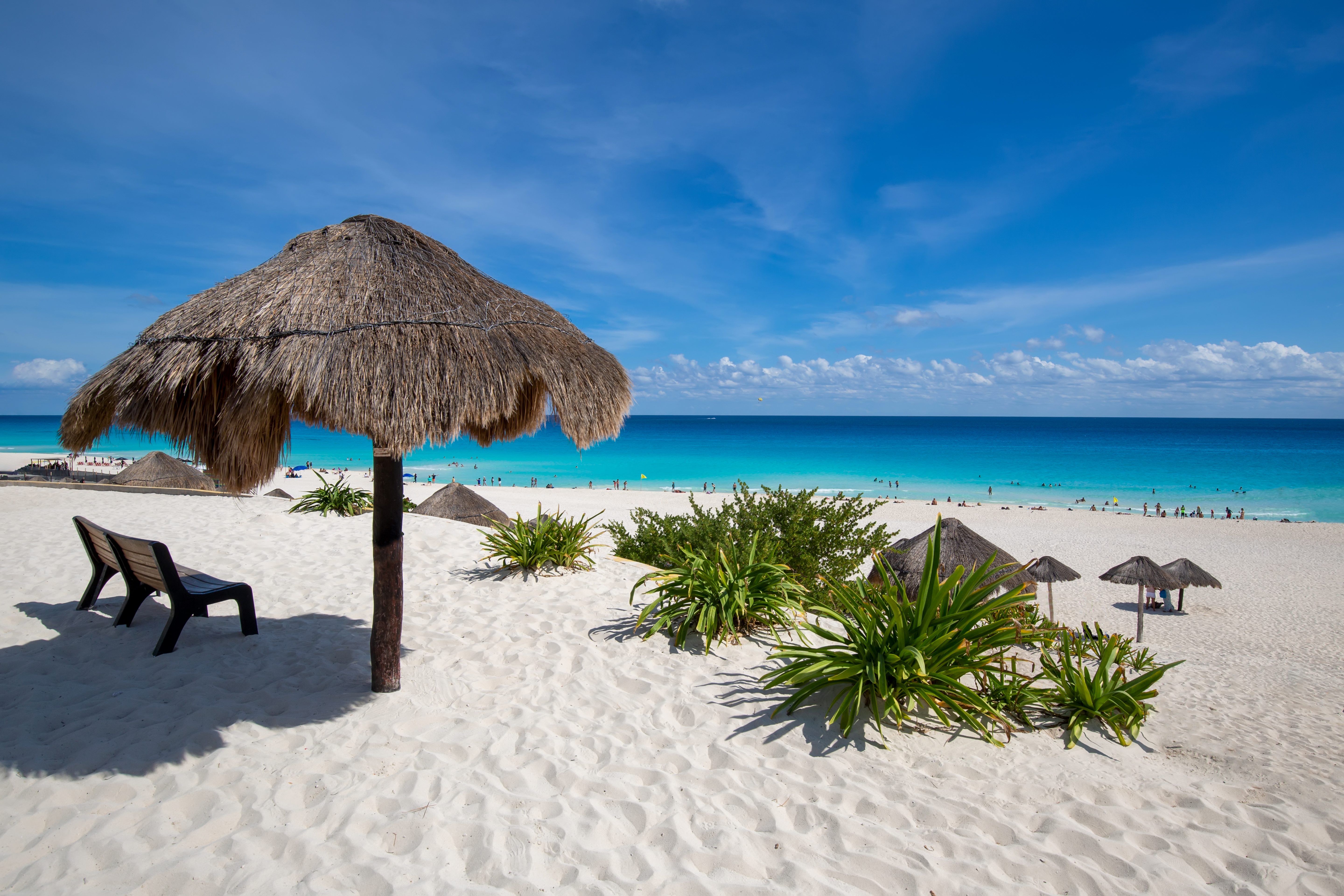 White sand beach, large palapa with bench, turquoise ocean, and blue sky.