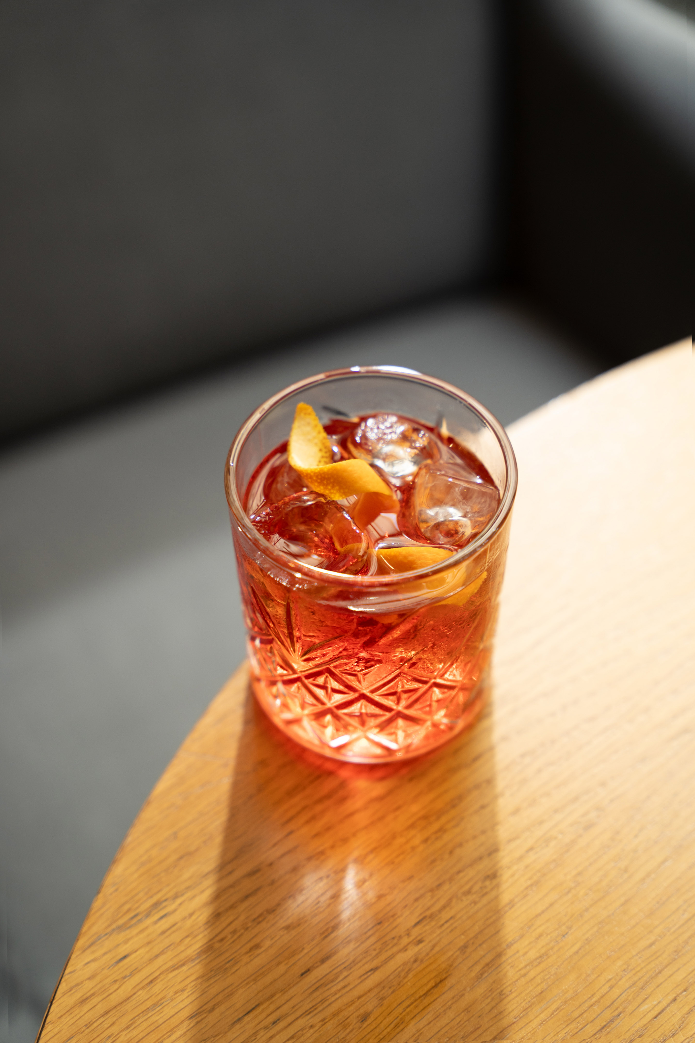 Negroni cocktail with orange peel and ice on a sunlit wooden table.