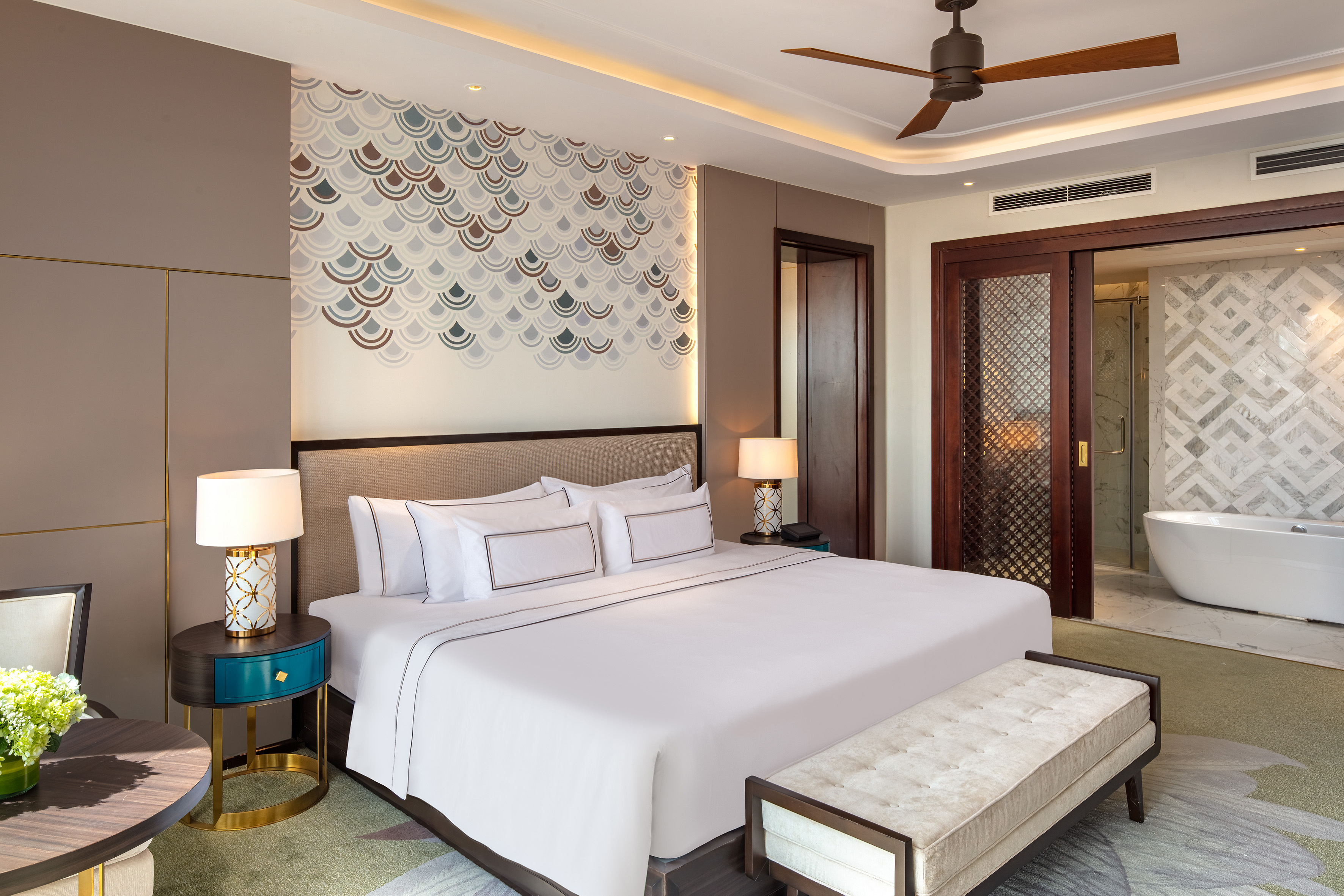Luxury hotel suite with king bed, patterned wall, and open ensuite bathroom.