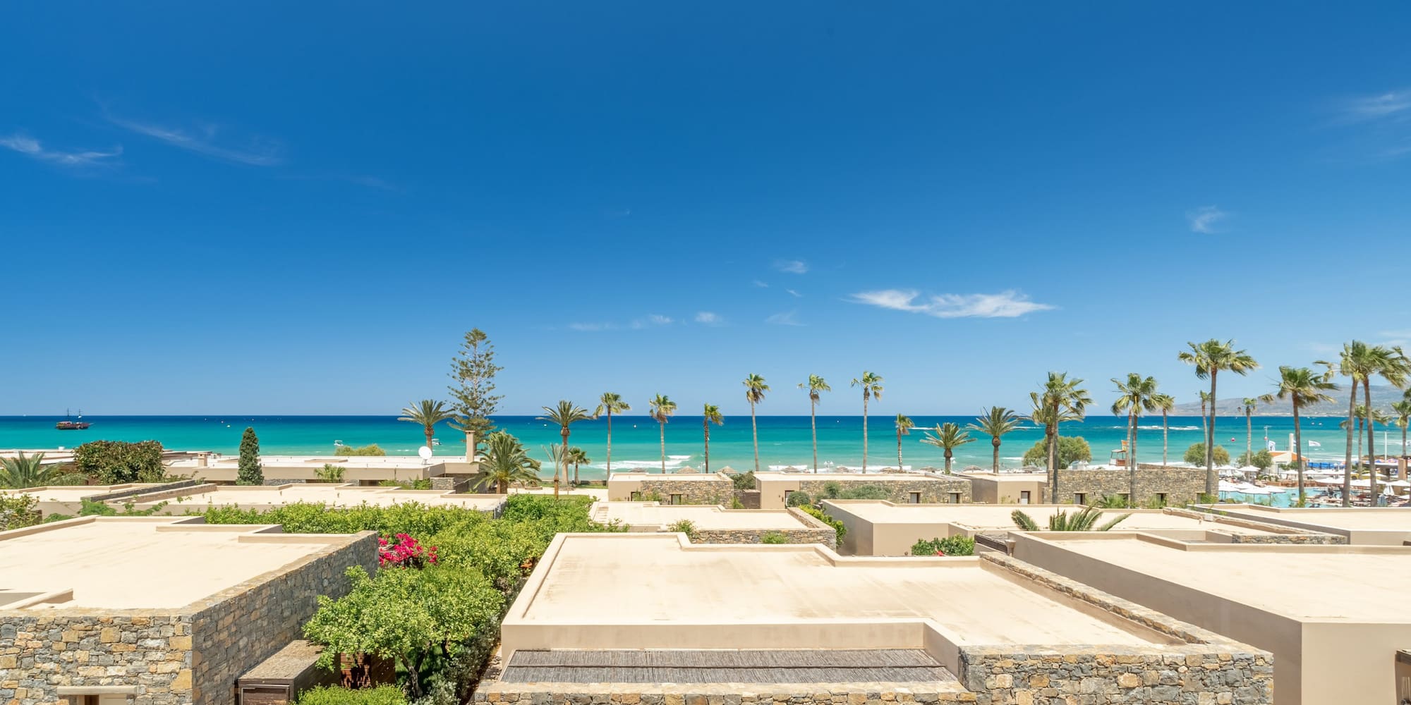 Beachfront stone villas, lush gardens, turquoise sea, and palm trees.