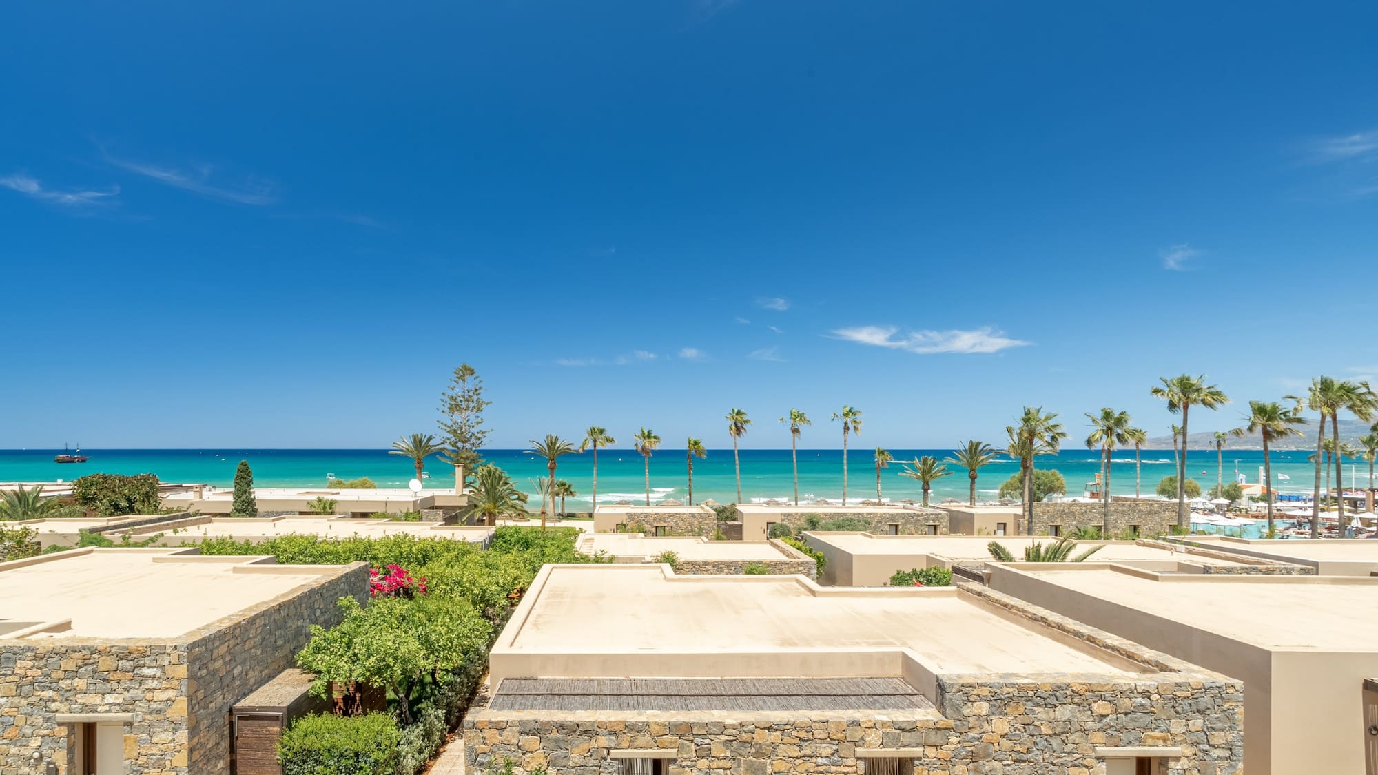 Beachfront stone villas, lush gardens, turquoise sea, and palm trees.