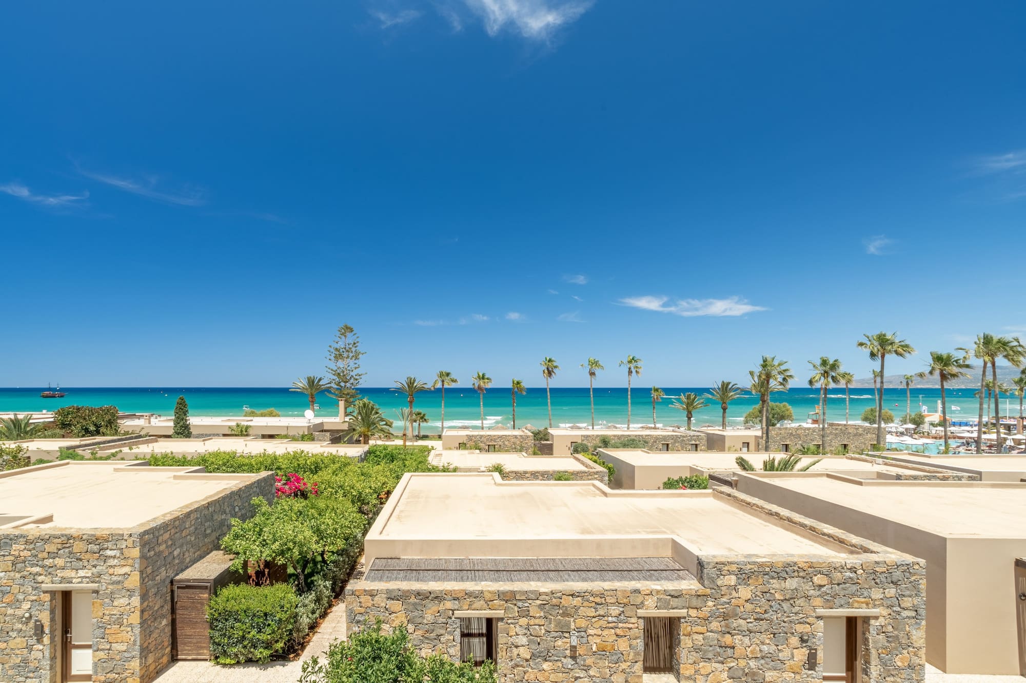Beachfront stone villas, lush gardens, turquoise sea, and palm trees.