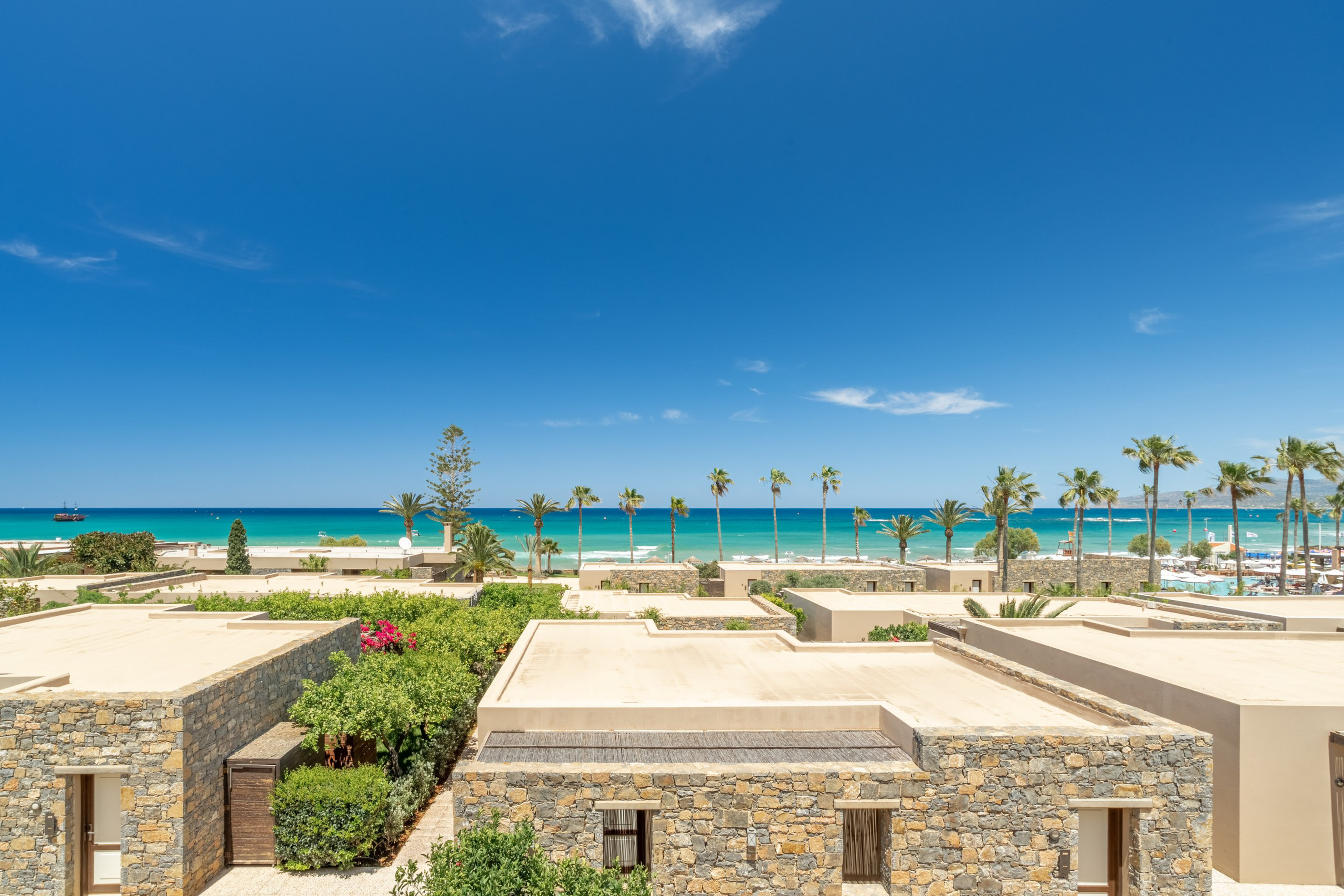 Beachfront stone villas, lush gardens, turquoise sea, and palm trees.