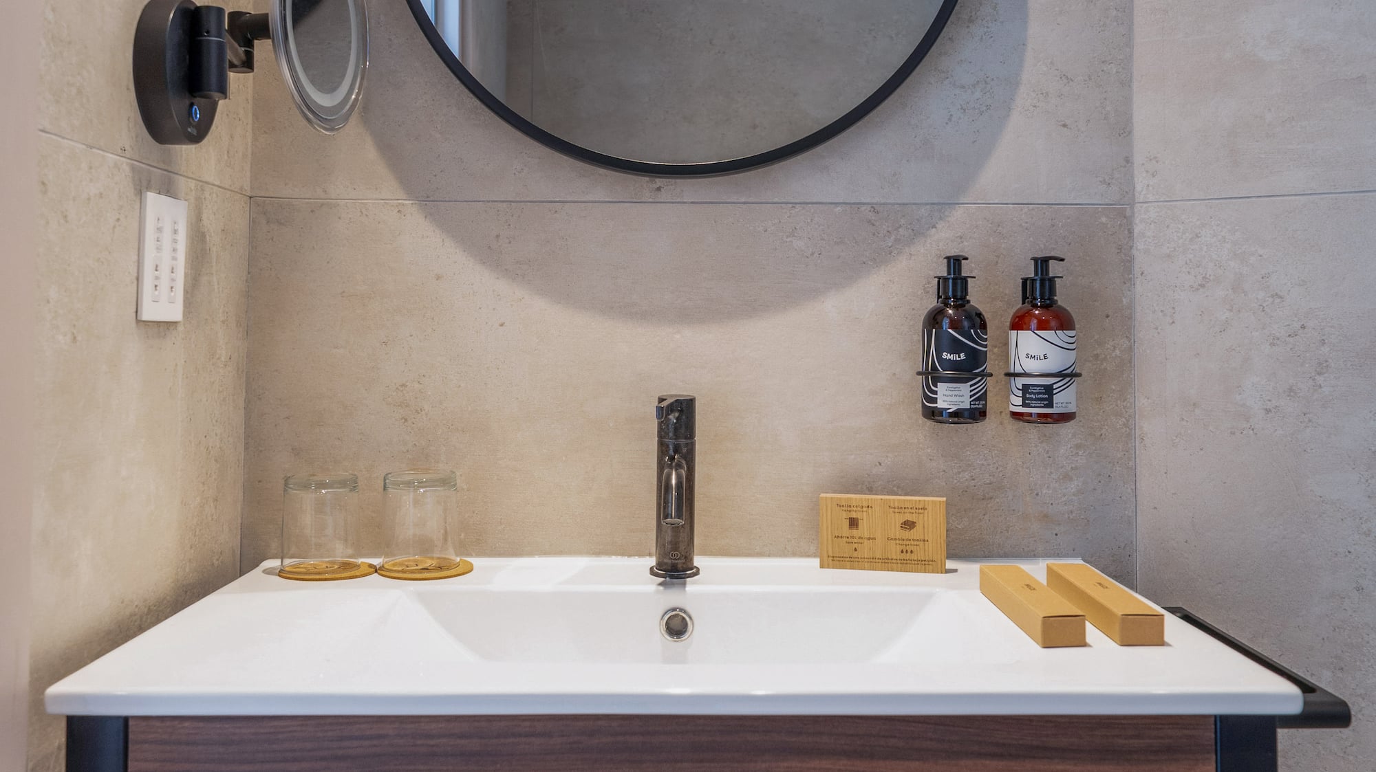 Modern hotel bathroom vanity, round mirror, wood, gray tiles, fresh towels.
