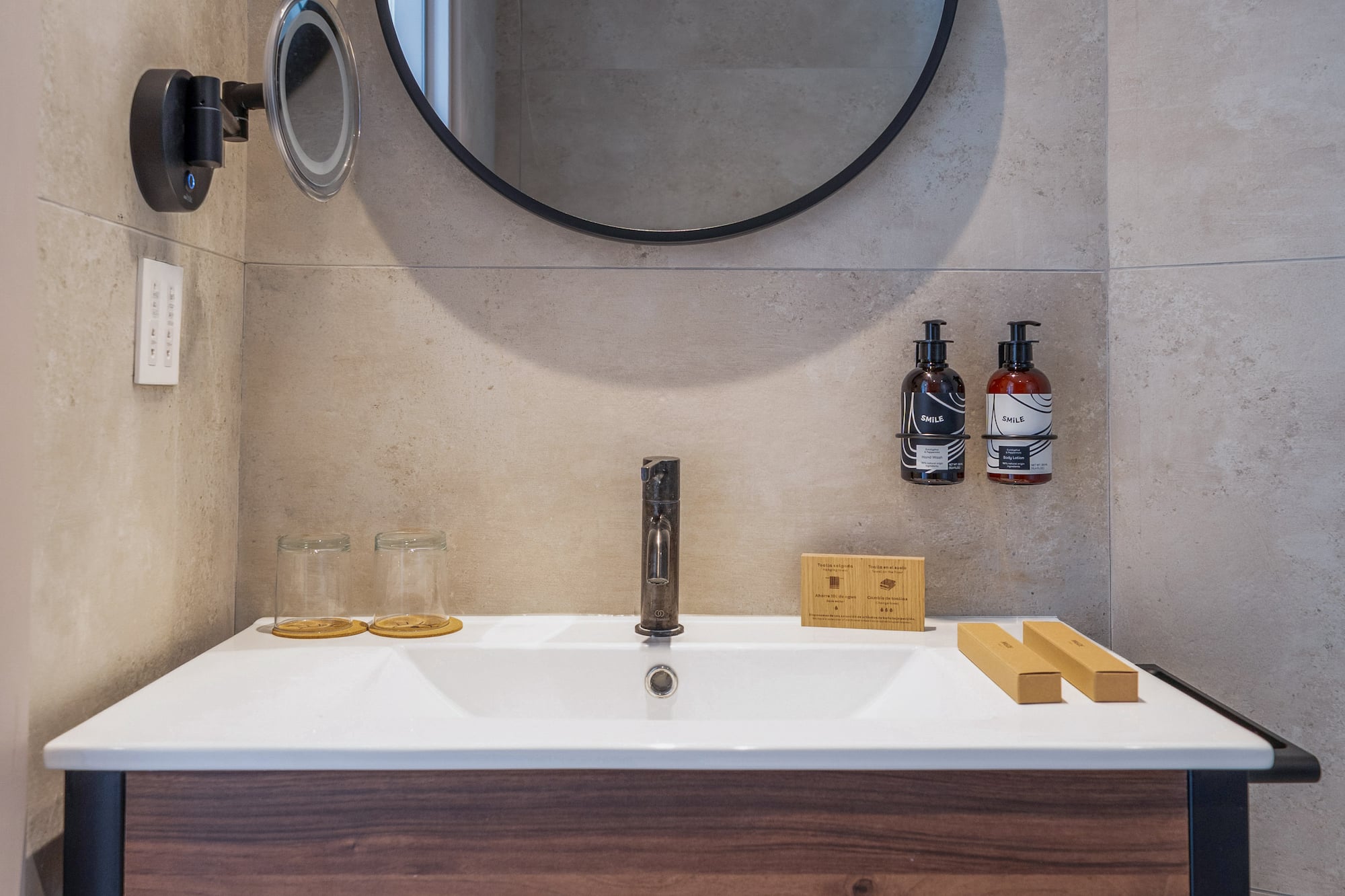 Modern hotel bathroom vanity, round mirror, wood, gray tiles, fresh towels.
