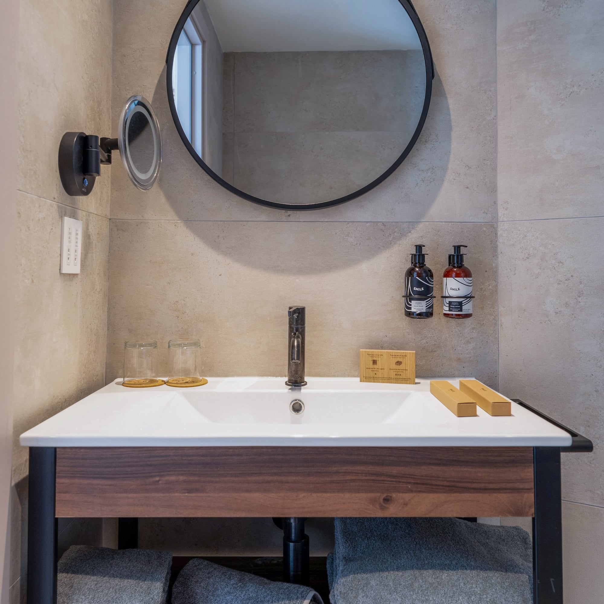 Modern hotel bathroom vanity, round mirror, wood, gray tiles, fresh towels.