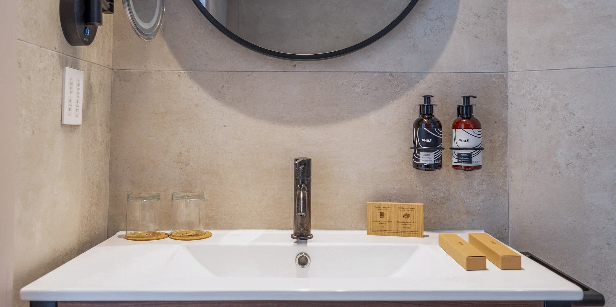 Modern hotel bathroom vanity, round mirror, wood, gray tiles, fresh towels.