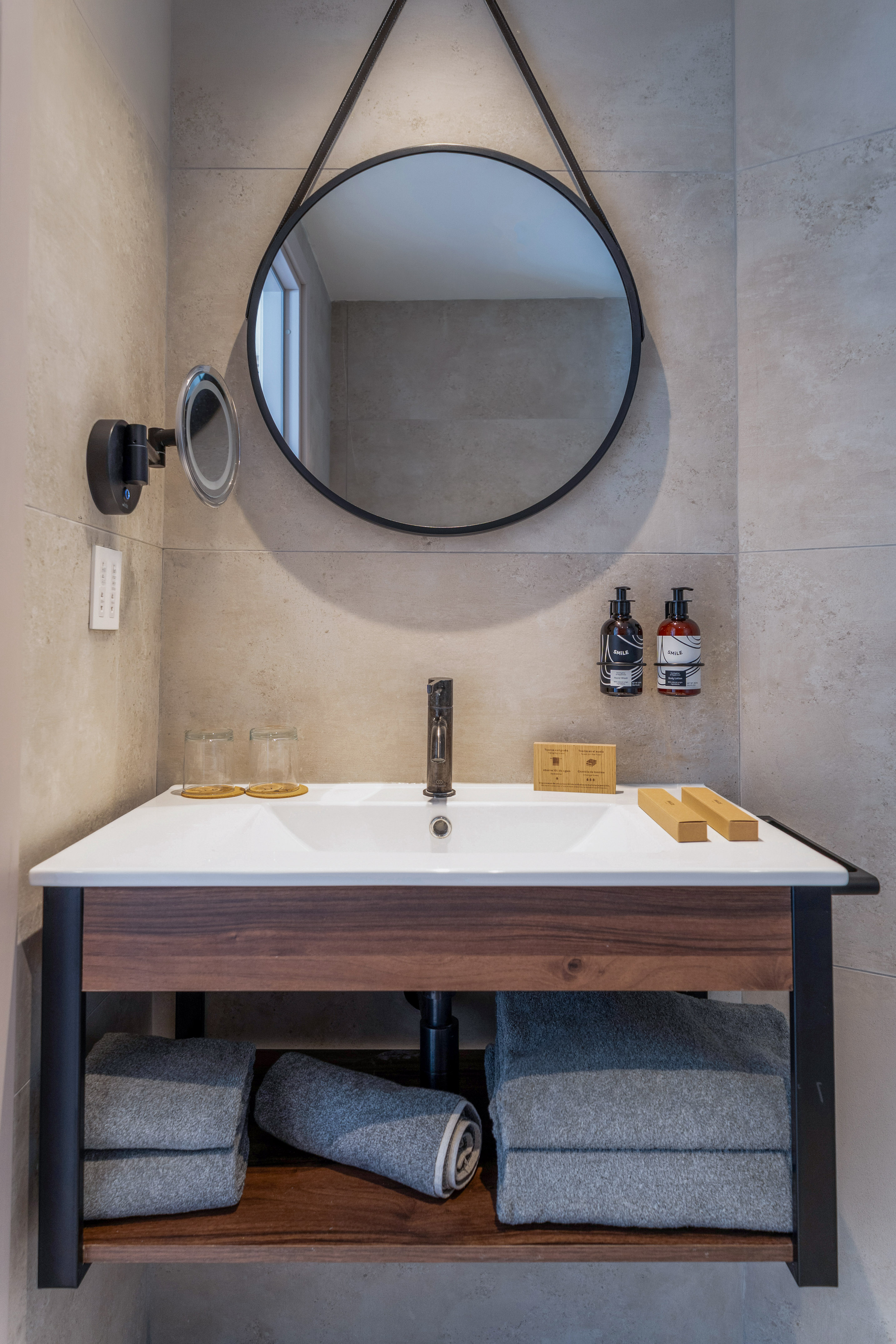 Modern hotel bathroom vanity, round mirror, wood, gray tiles, fresh towels.