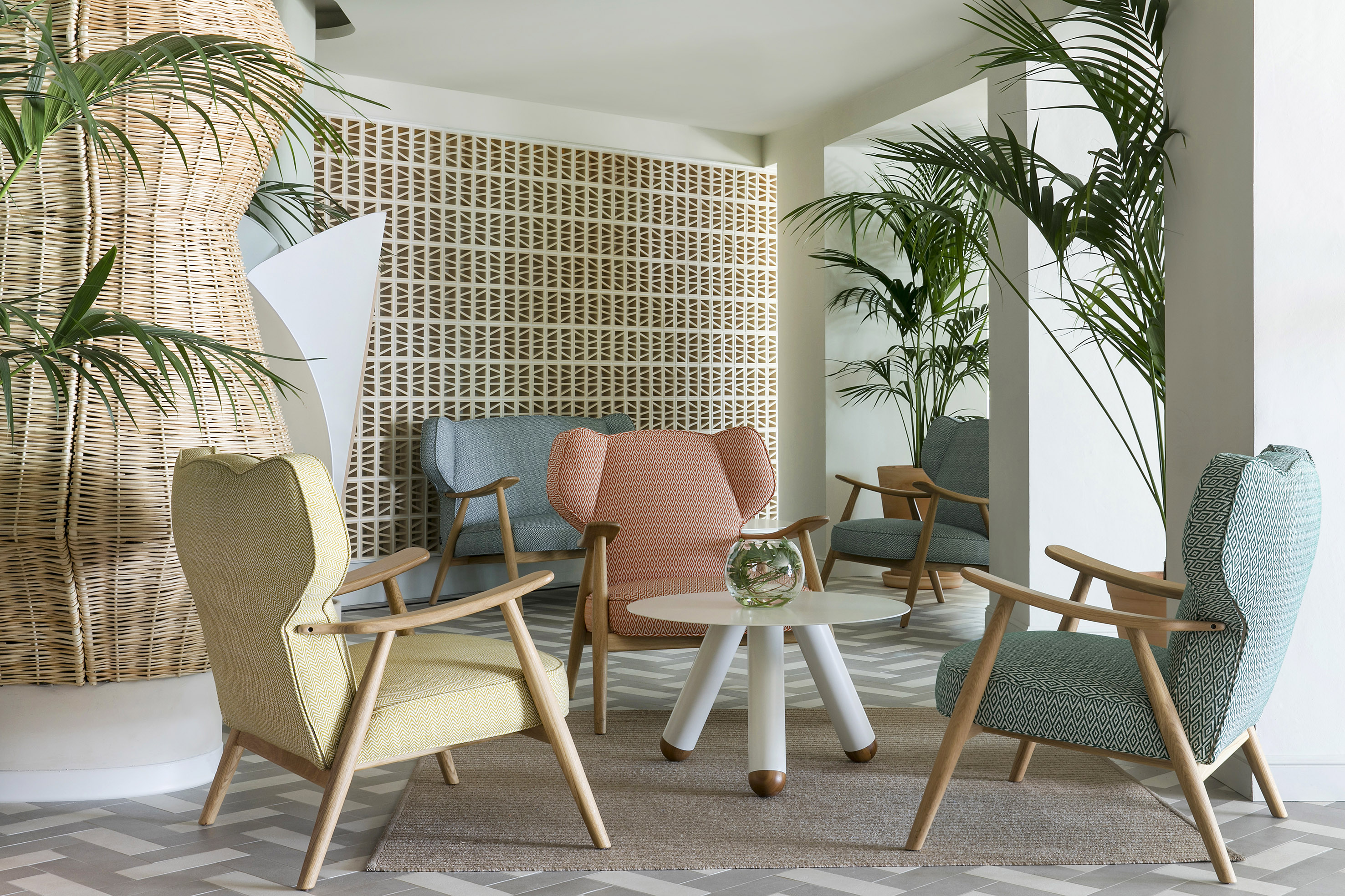 Colorful lounge with armchairs, geometric wall, rattan column, tropical plants.